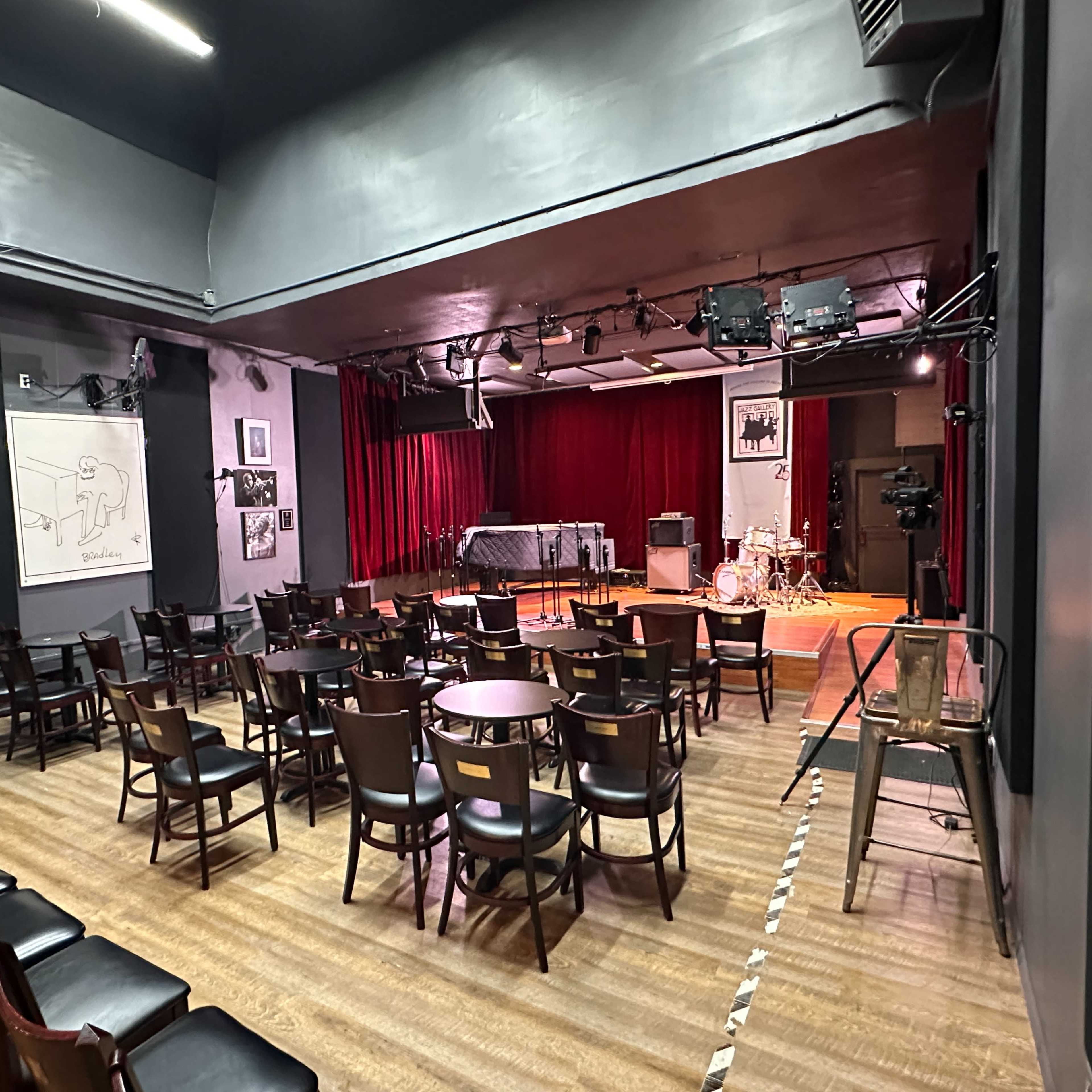 A small performance venue with a stage, red curtains, and rows of chairs set up for an audience.