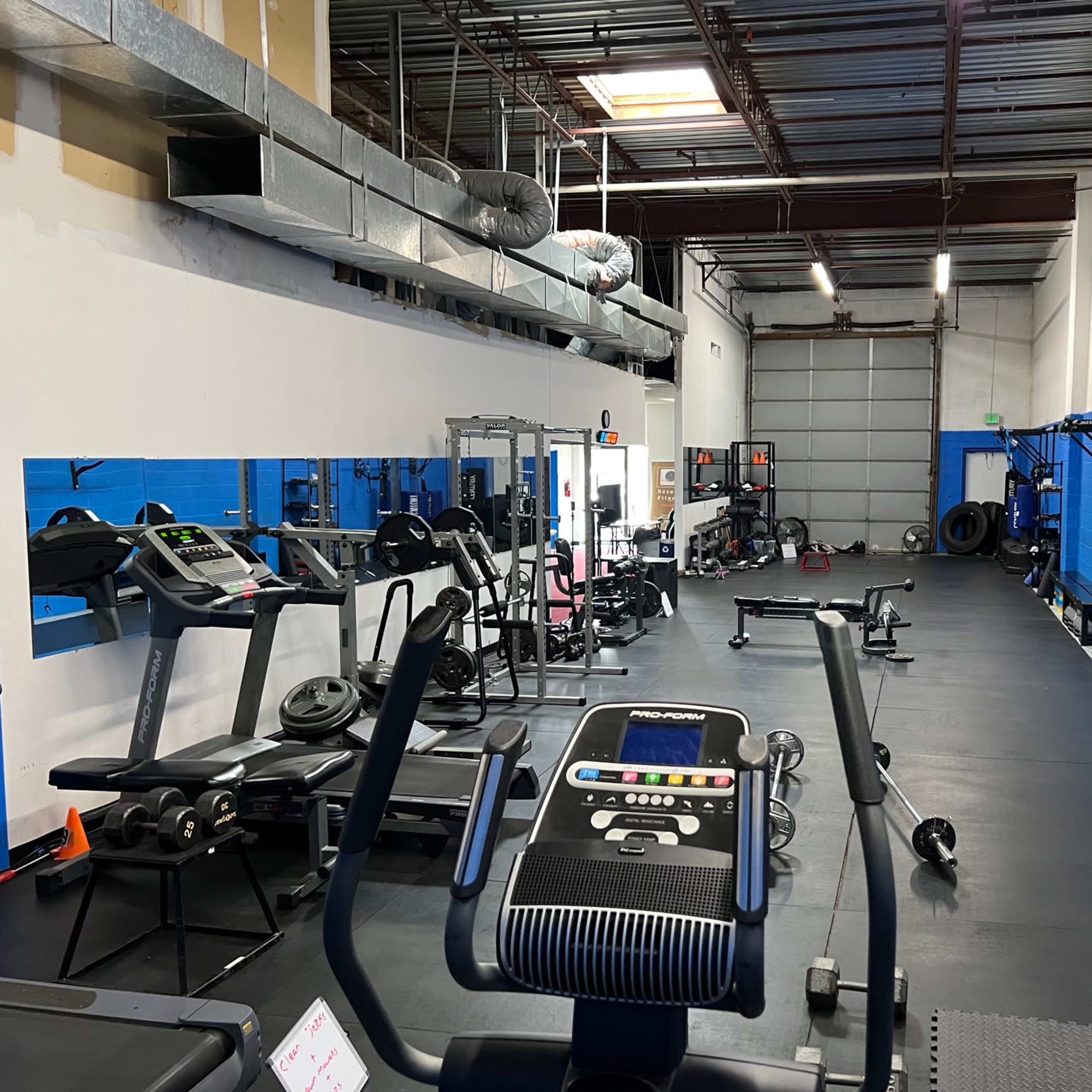 A fitness gym with various exercise machines, weights, and equipment arranged along the walls and floor.