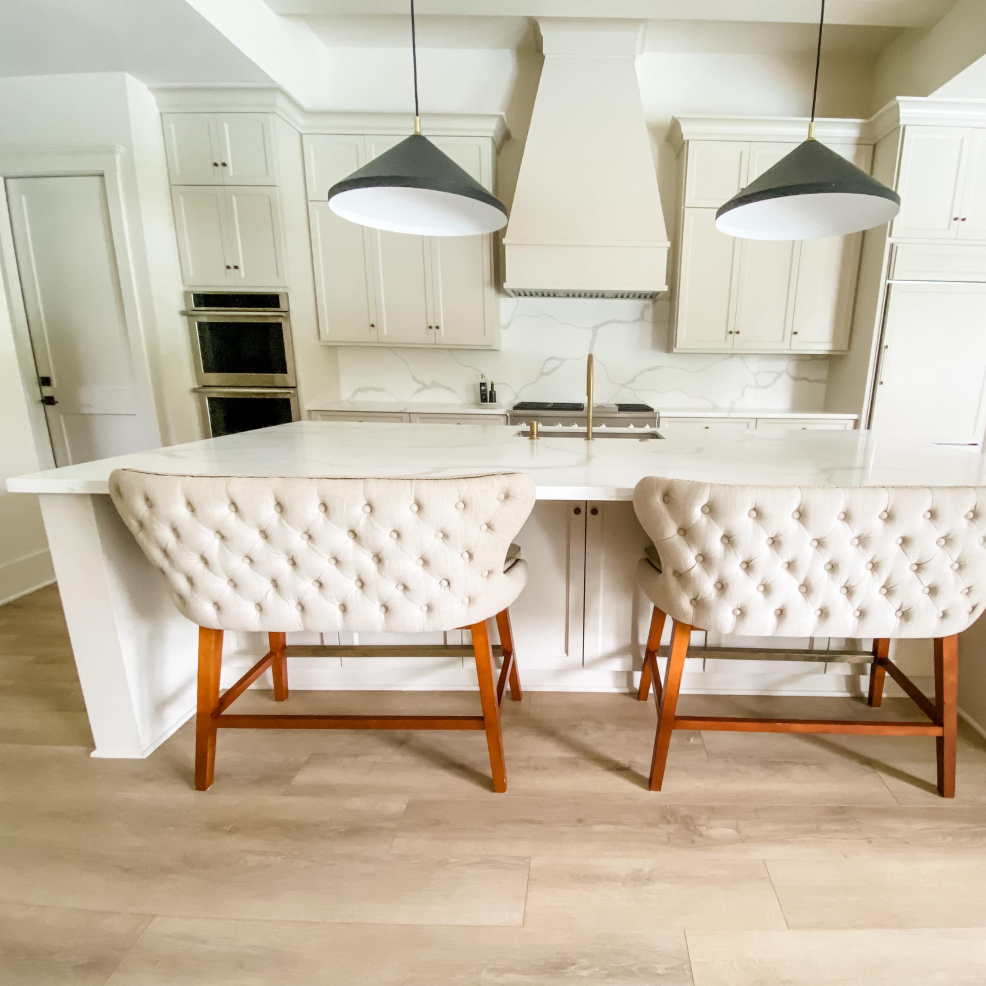 A modern kitchen with a central island featuring two tufted bar stools and pendant lighting above.