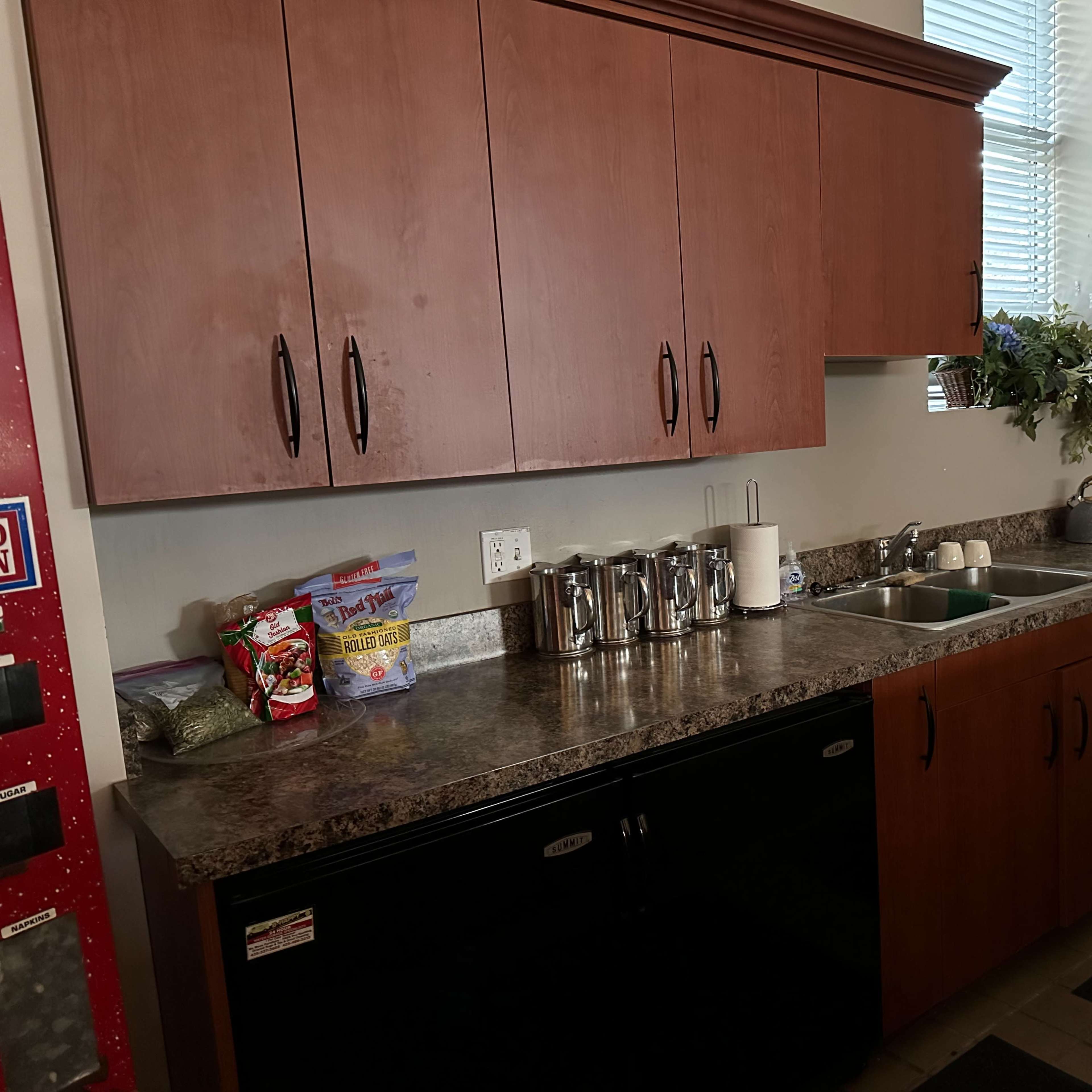 A kitchen countertop with cabinets above, featuring a sink, kitchen appliances, and a variety of food items arranged on the surface.