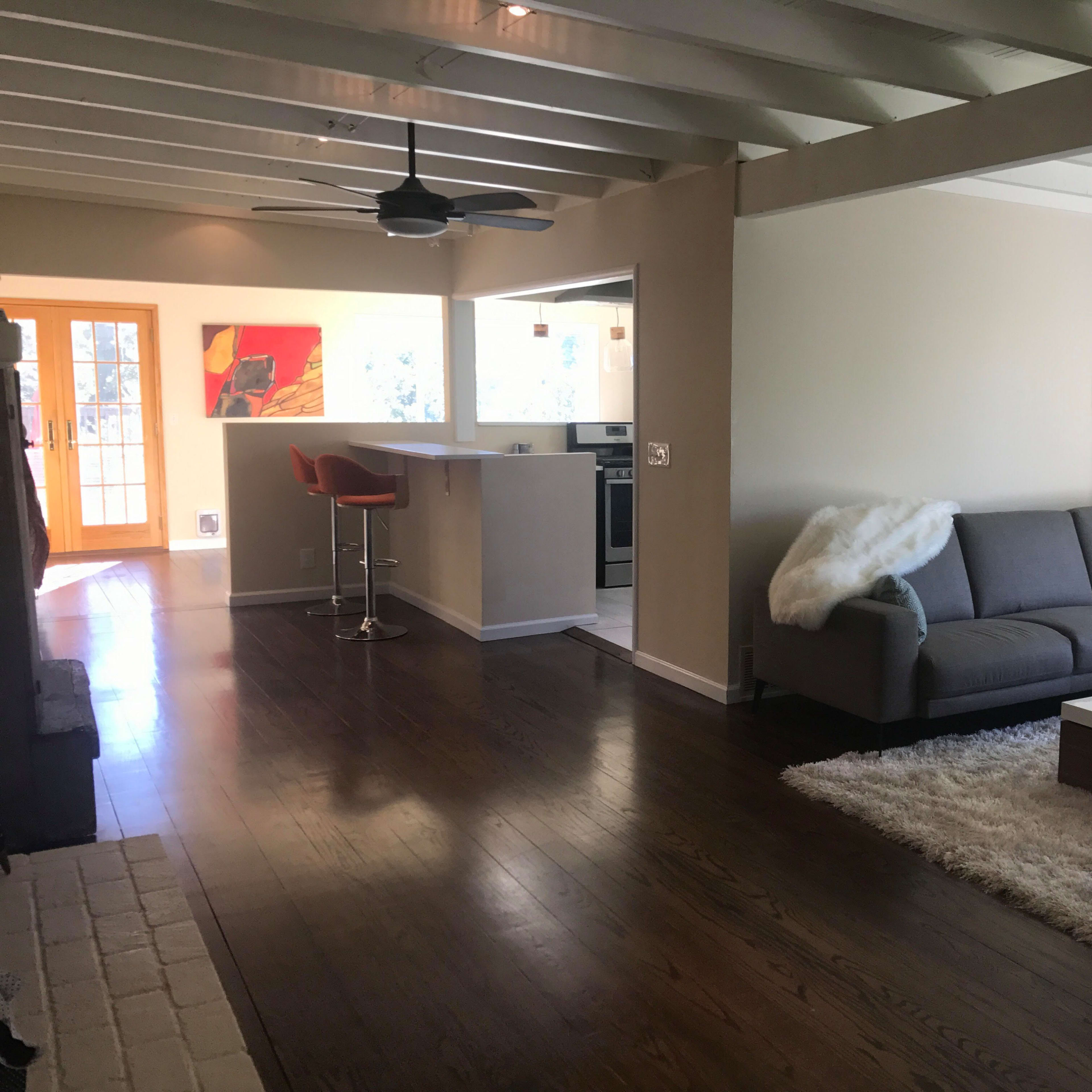 A spacious living room features a gray sofa, a coffee table on a plush rug, and a view of an open kitchen with bar seating.