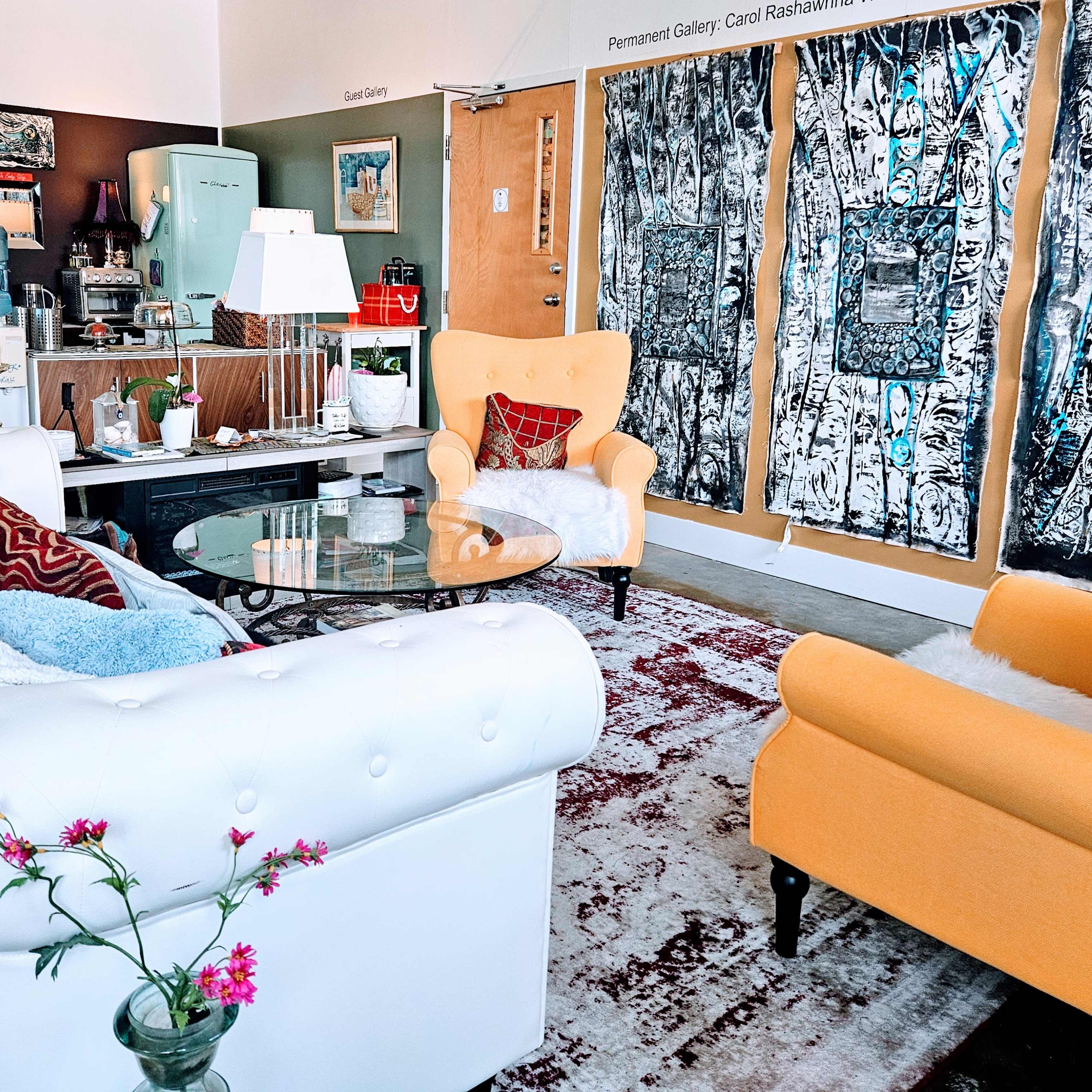 A stylish living area with a white tufted sofa, yellow armchair, a glass coffee table, artwork on the wall, and various decorative items.