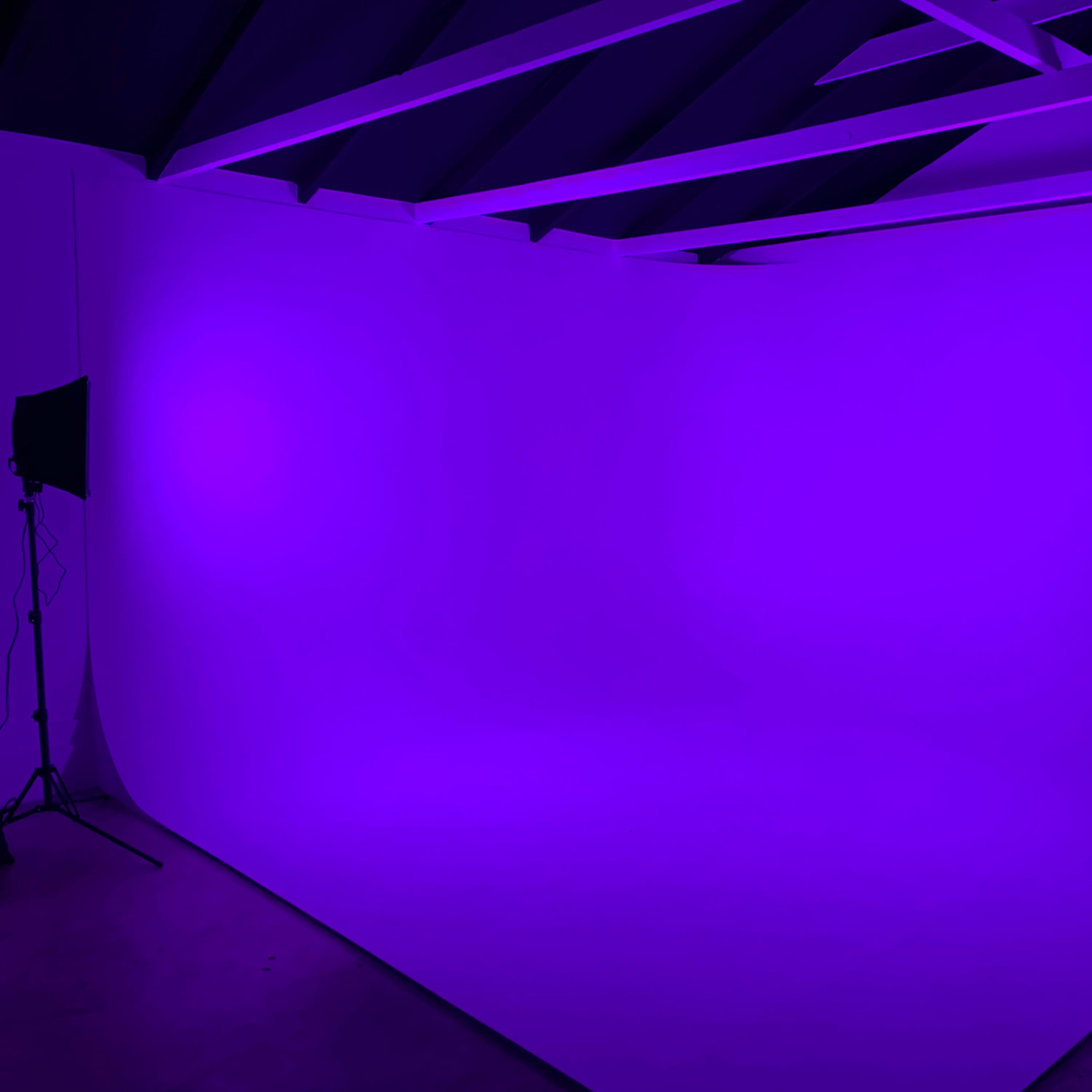 A minimalist studio space with a purple backdrop and lighting, featuring exposed beams on the ceiling.