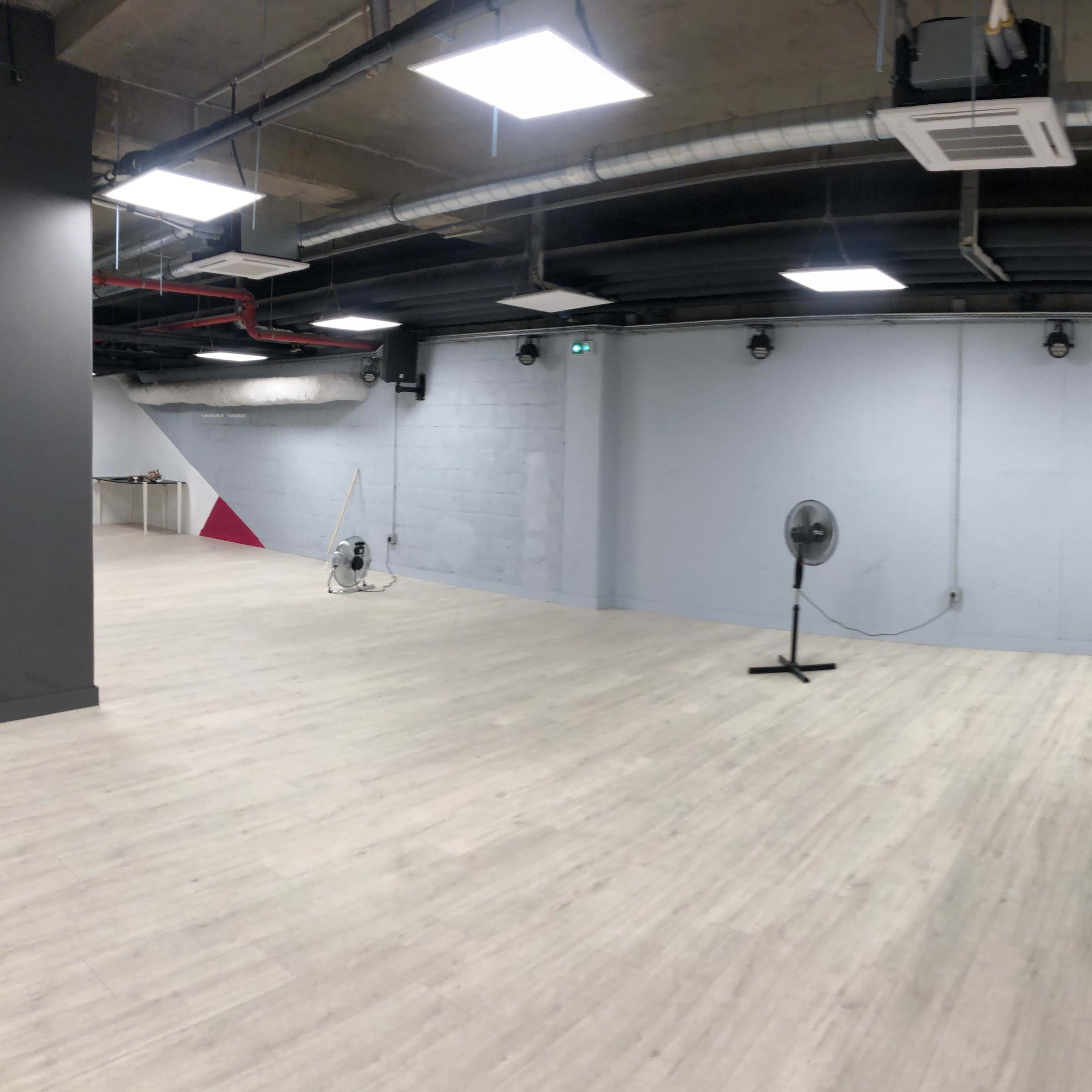 An empty industrial-style room with light wooden flooring and a wall featuring a geometric pattern of black and red sections.