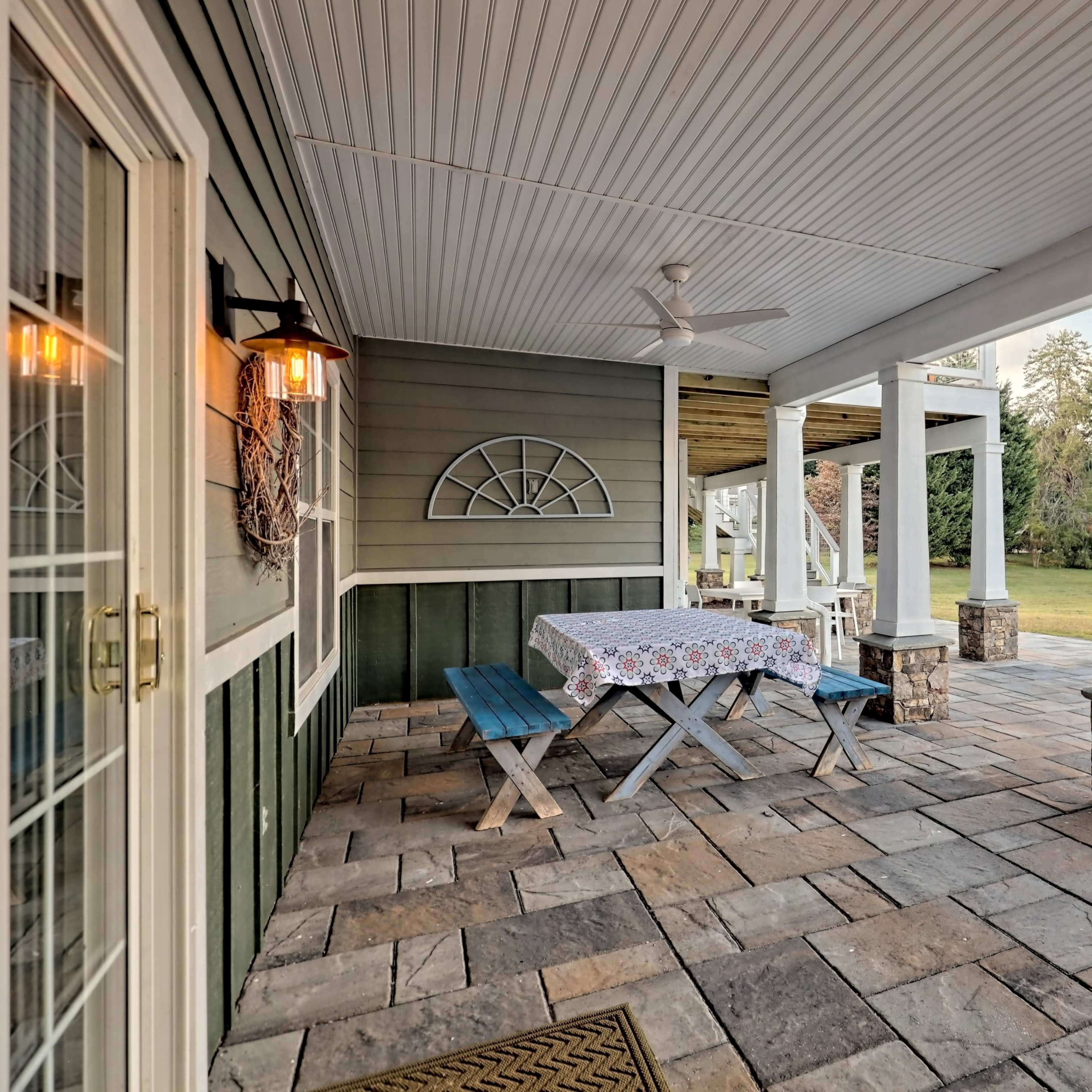 A covered patio area with a stone floor, a table covered with a patterned cloth, and blue benches.