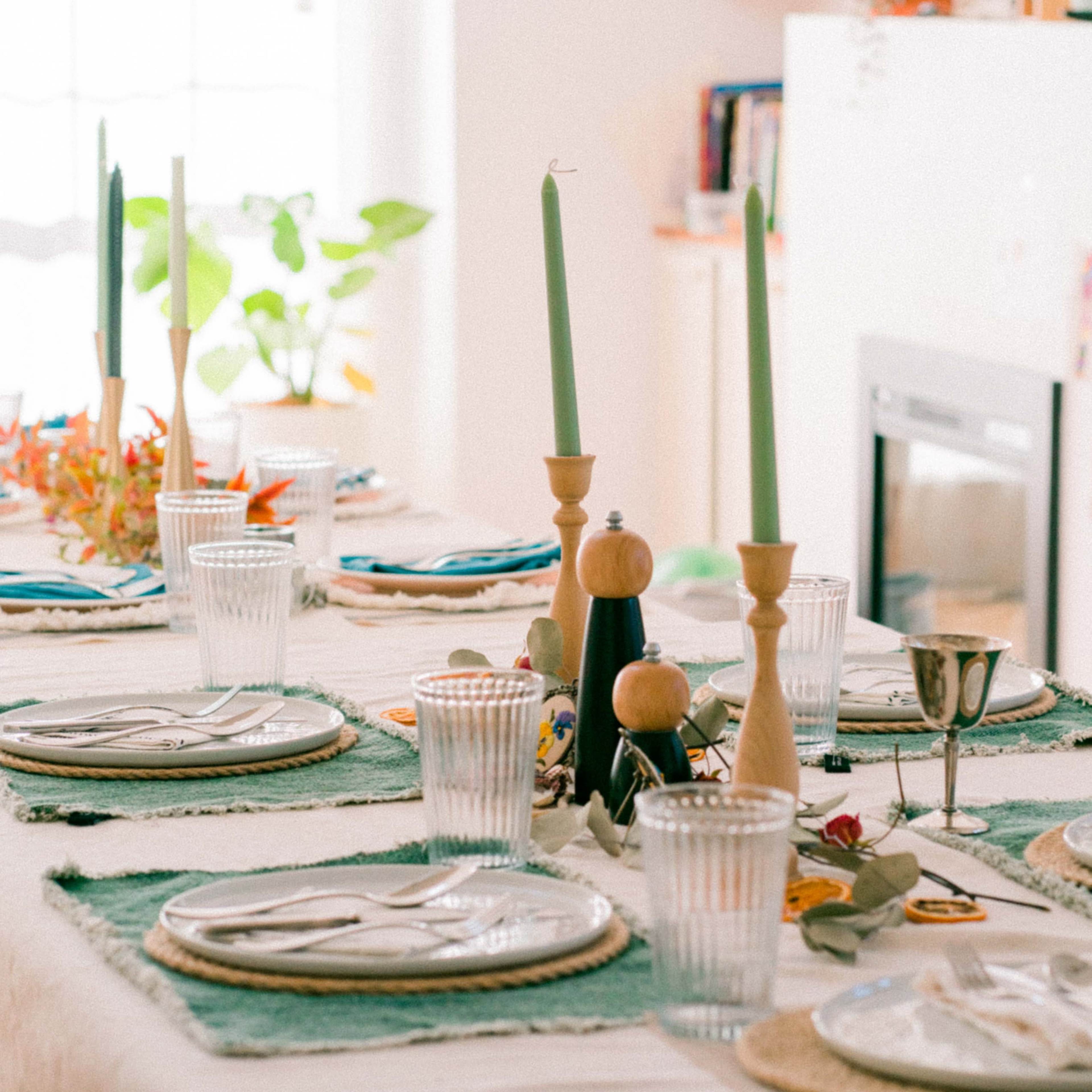 A dining table is set with plates, glasses, cutlery, and decorative candles in a bright, modern room.