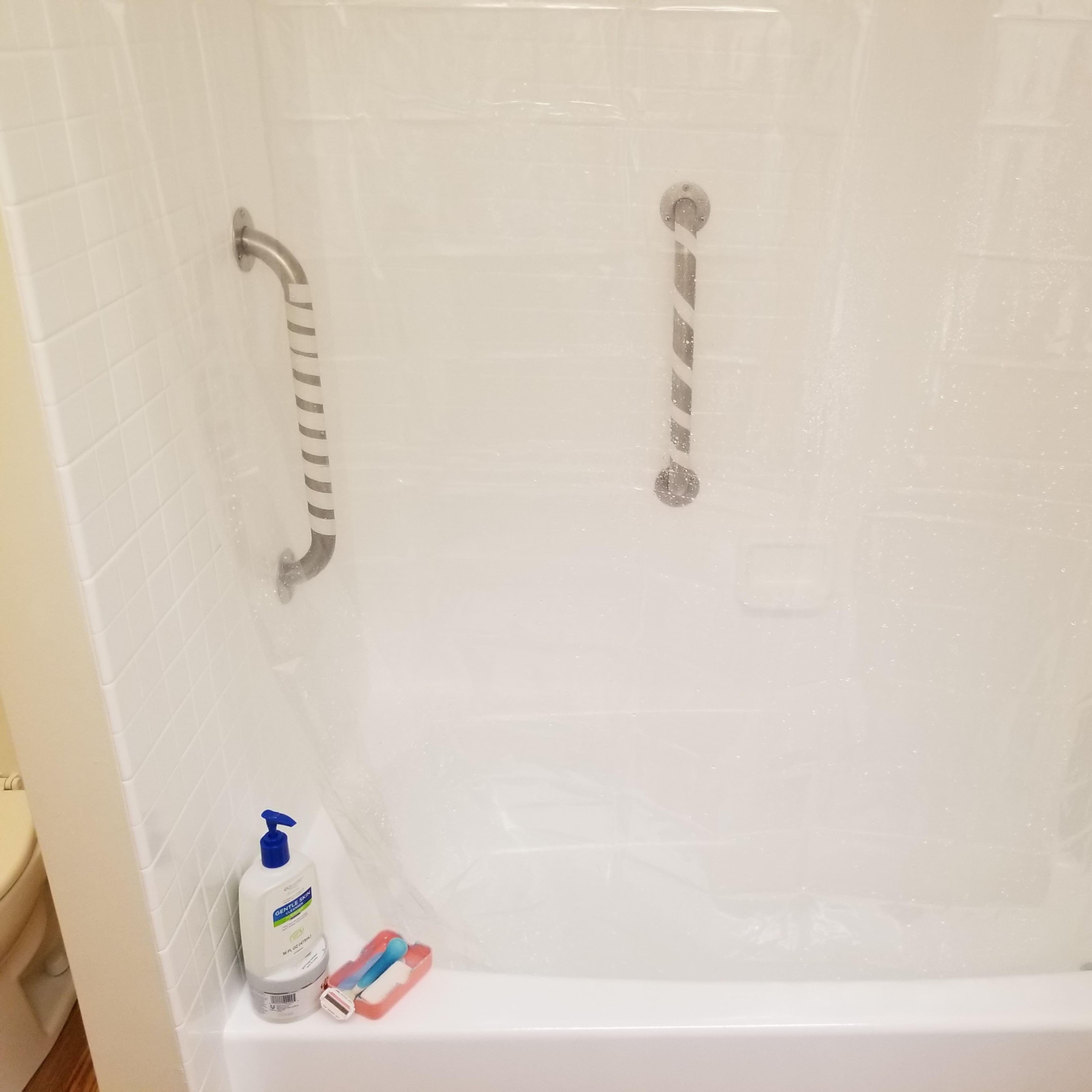 A shower stall with white tiles and a translucent curtain, featuring various toiletries placed around the tub.