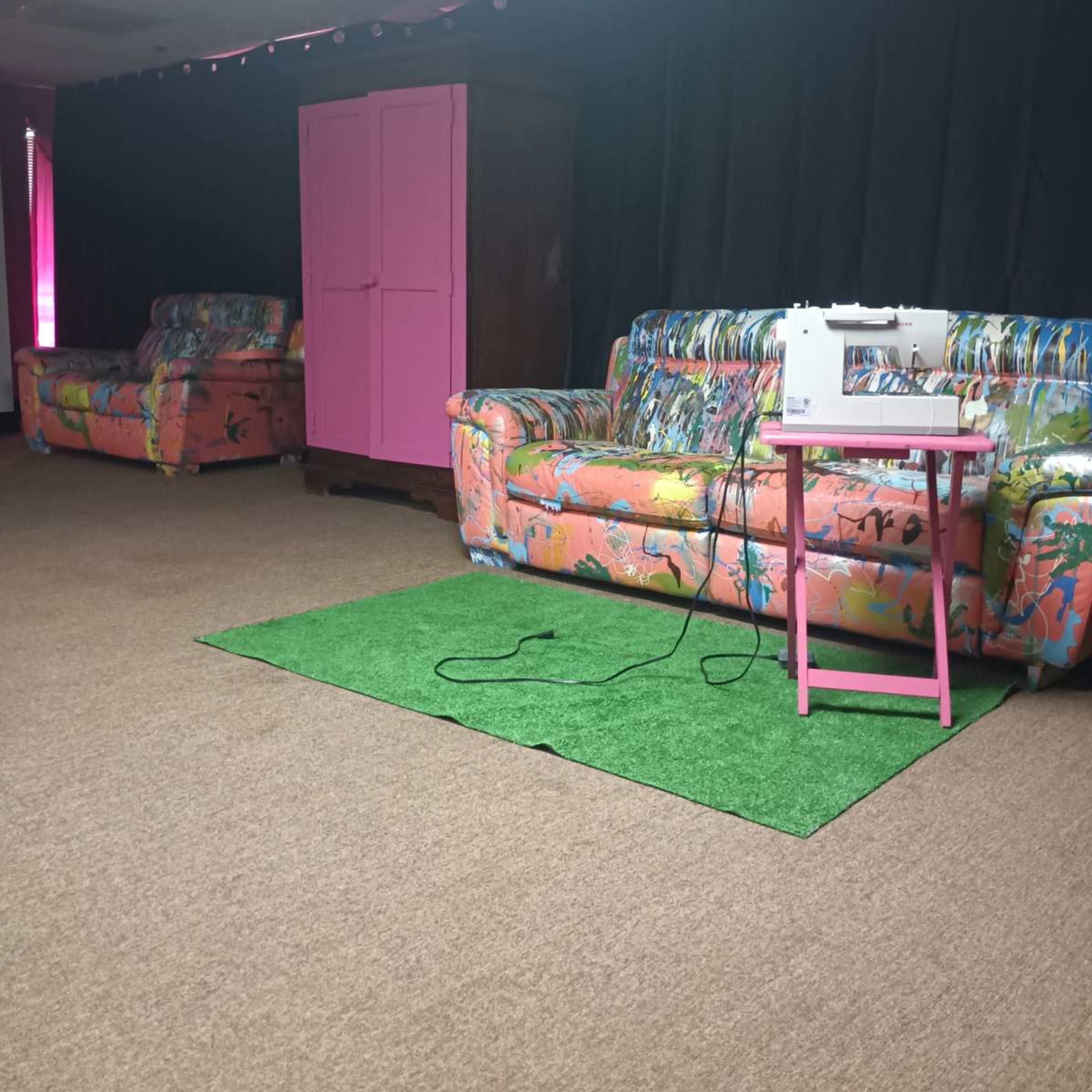 A room with two colorful couches, a pink side table with a sewing machine, and a dark backdrop.