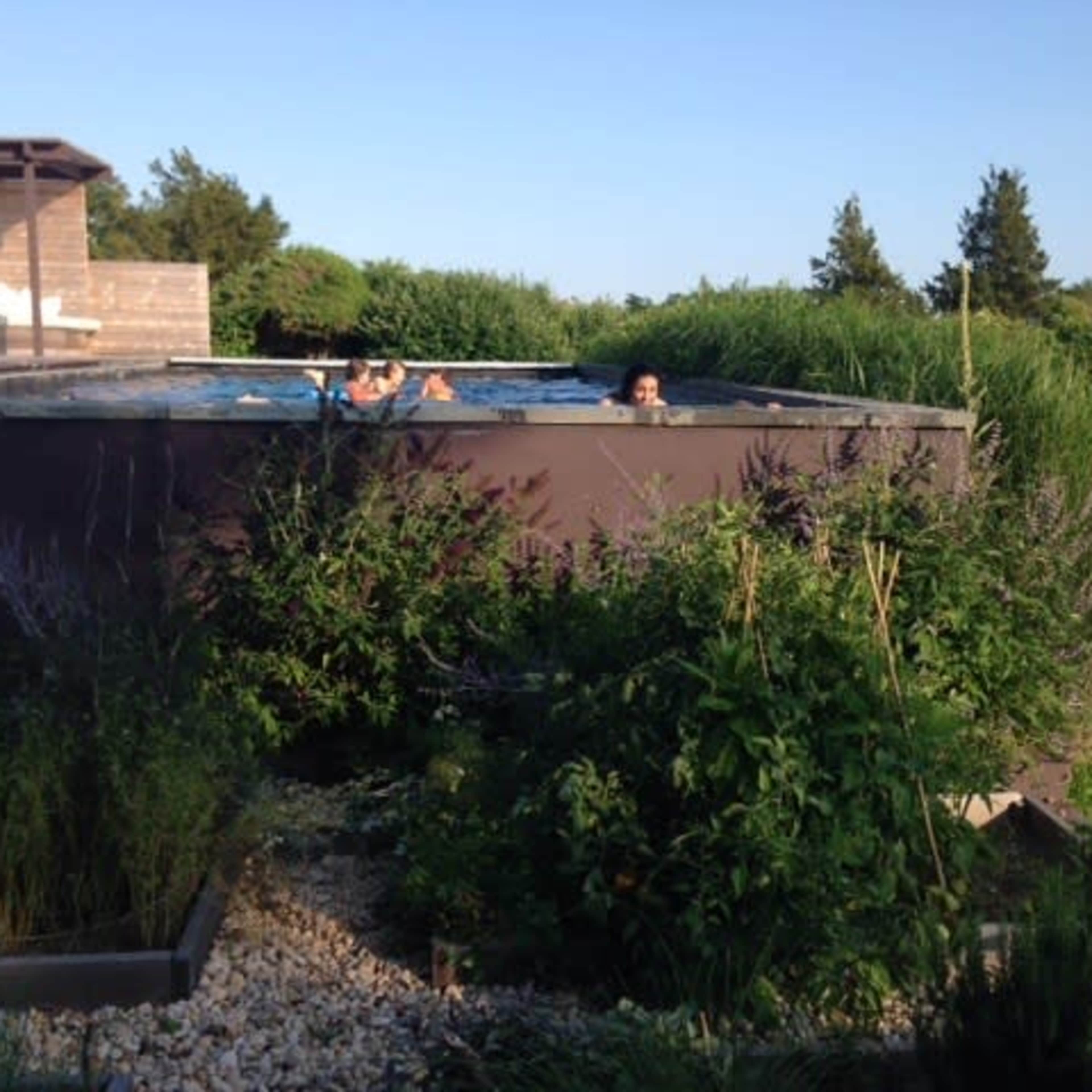 Two people are sitting in a hot tub surrounded by green shrubbery and a gravel garden.
