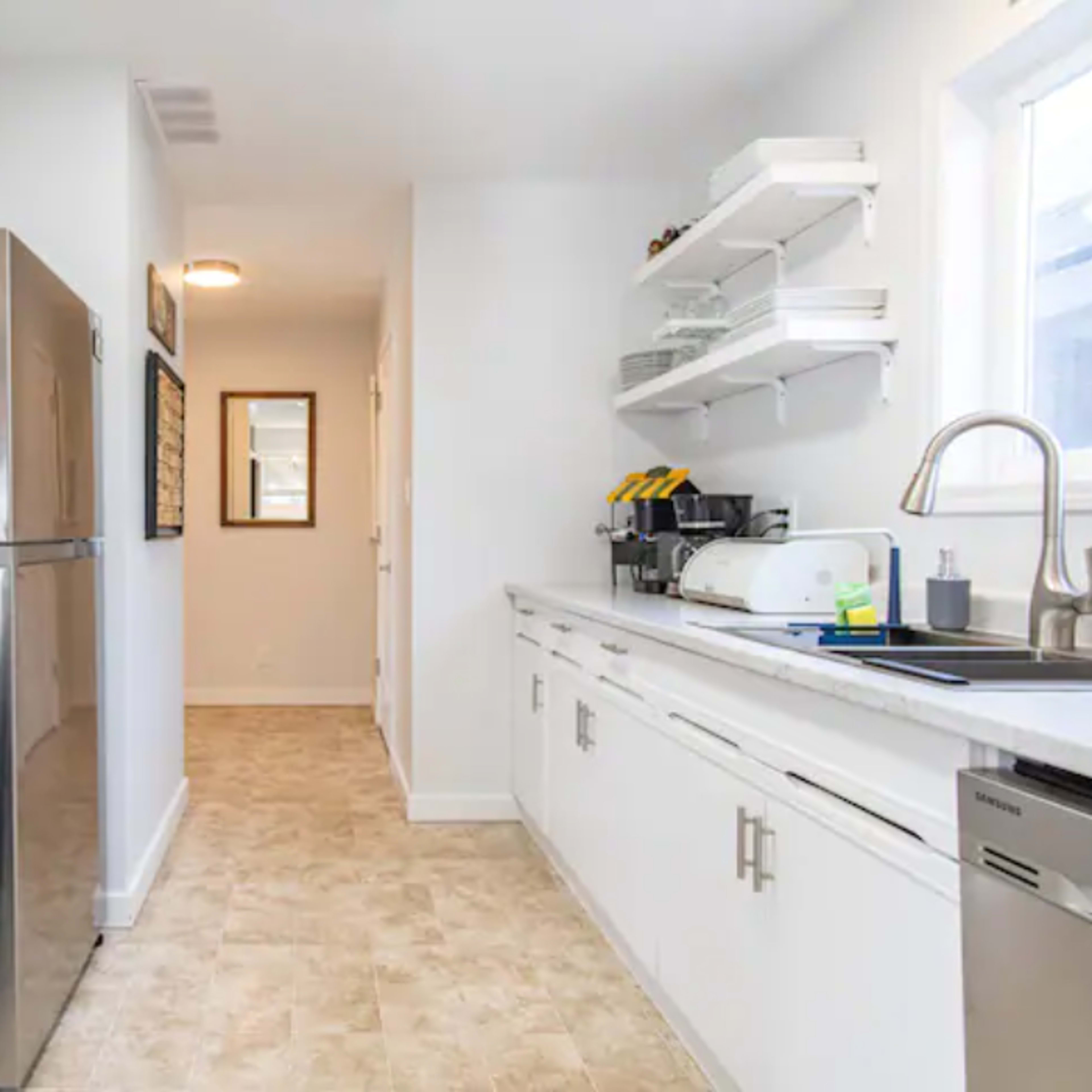 A modern kitchen with white cabinetry, stainless steel appliances, and a narrow hallway leading to another room.