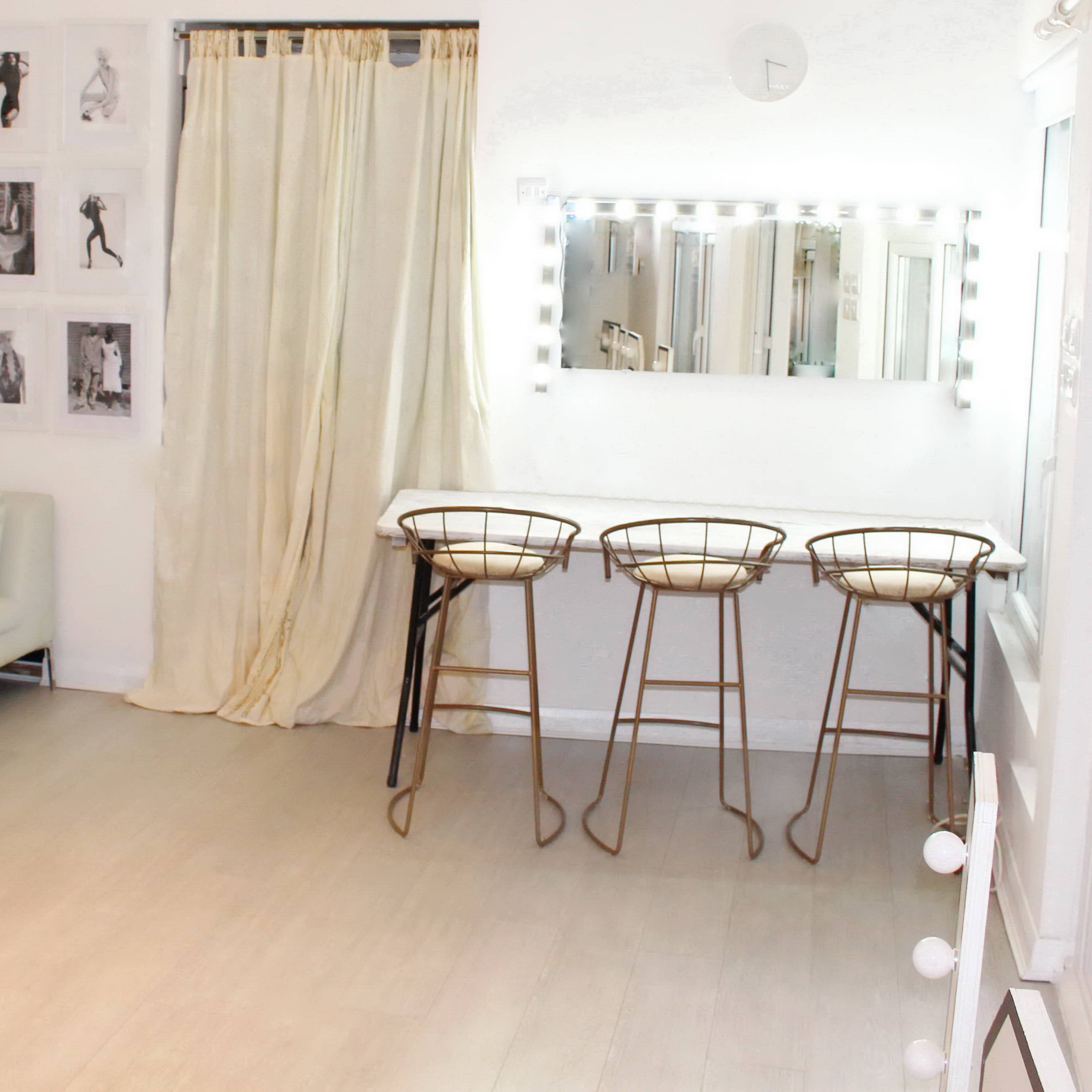 A spacious room with a light-colored sofa, a bar counter with three stools, and a wall adorned with black and white photographs.