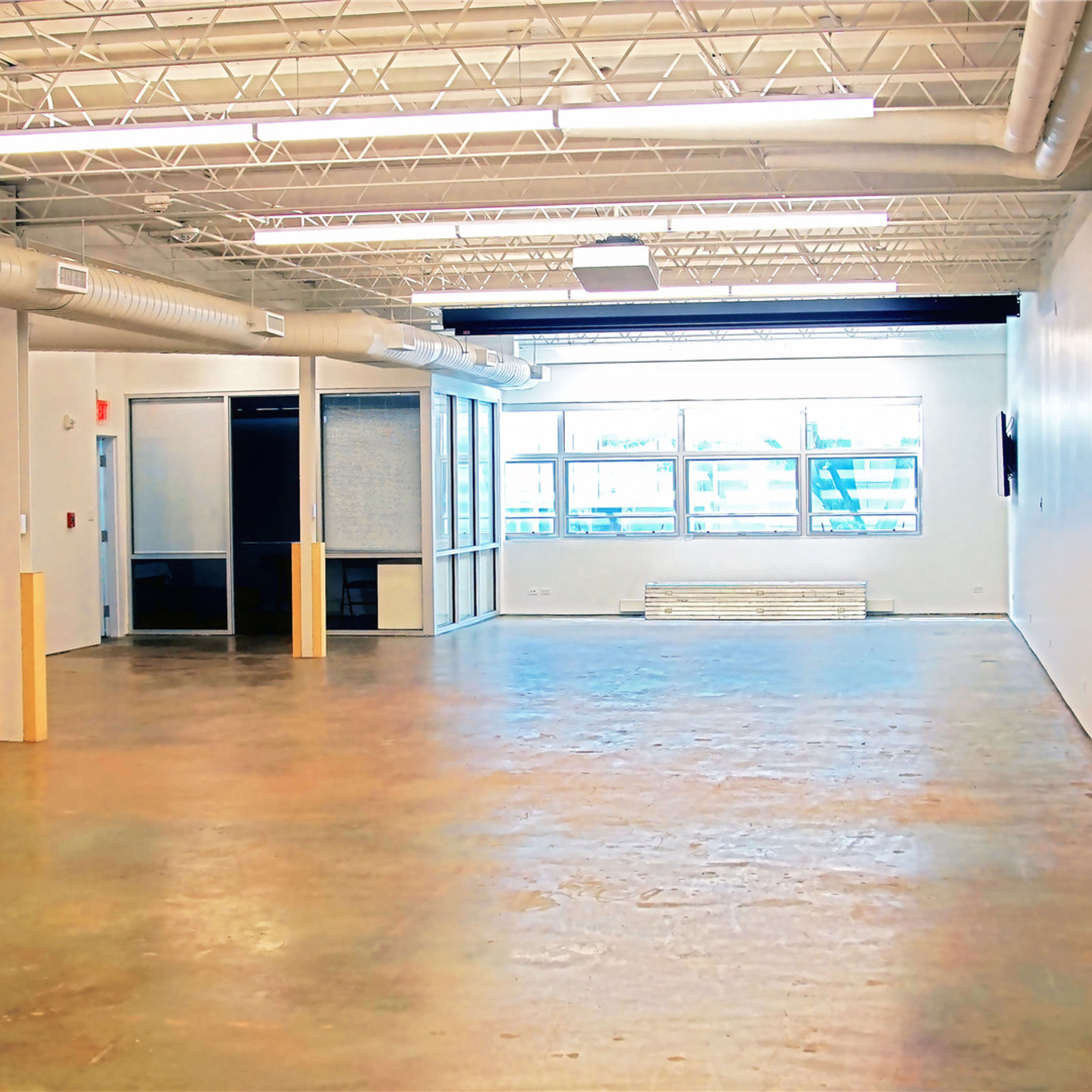 A spacious industrial-style room with polished concrete flooring and large windows allowing natural light to enter.