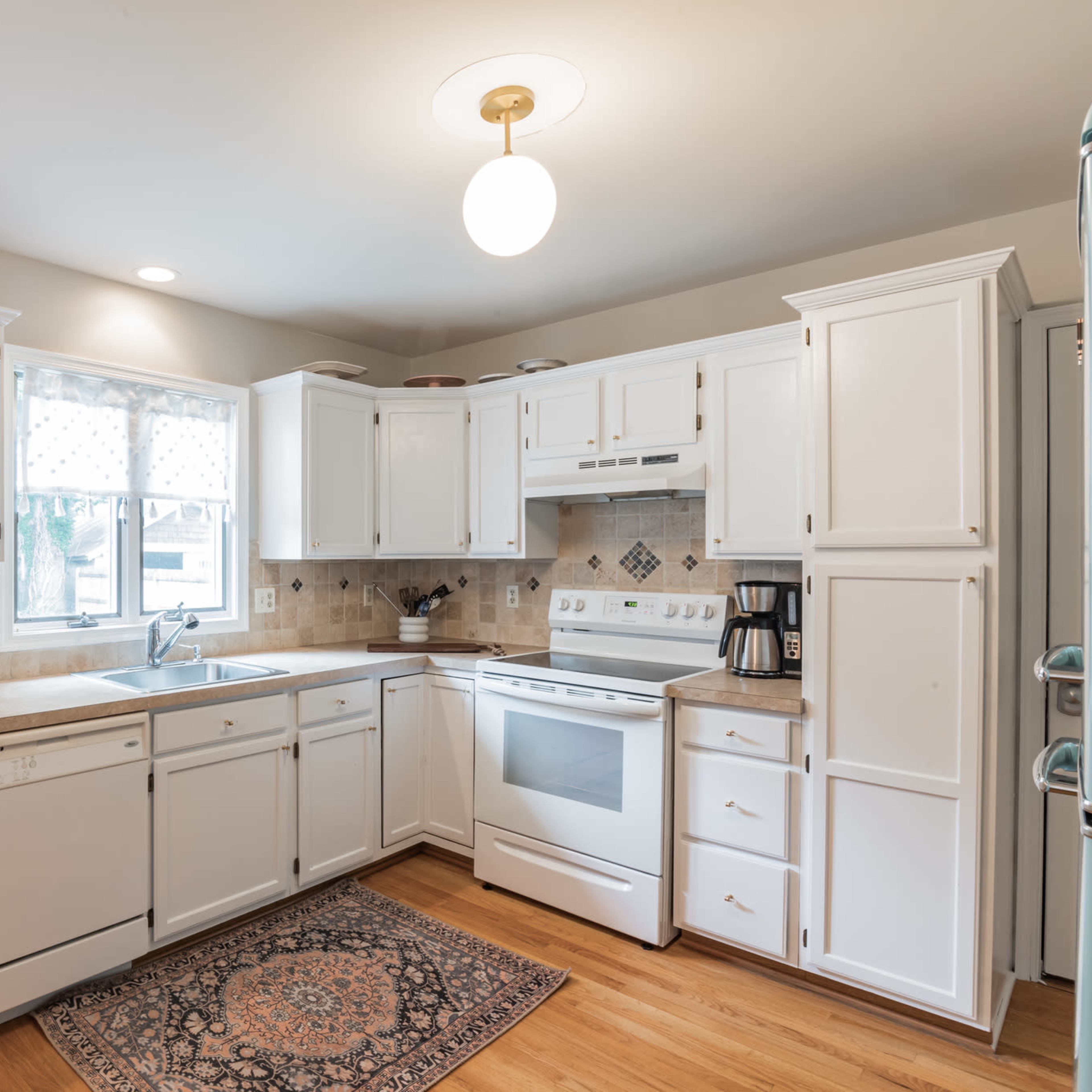 A bright kitchen features white cabinets, a light-colored countertop, and appliances including a stove, microwave, and coffee maker.