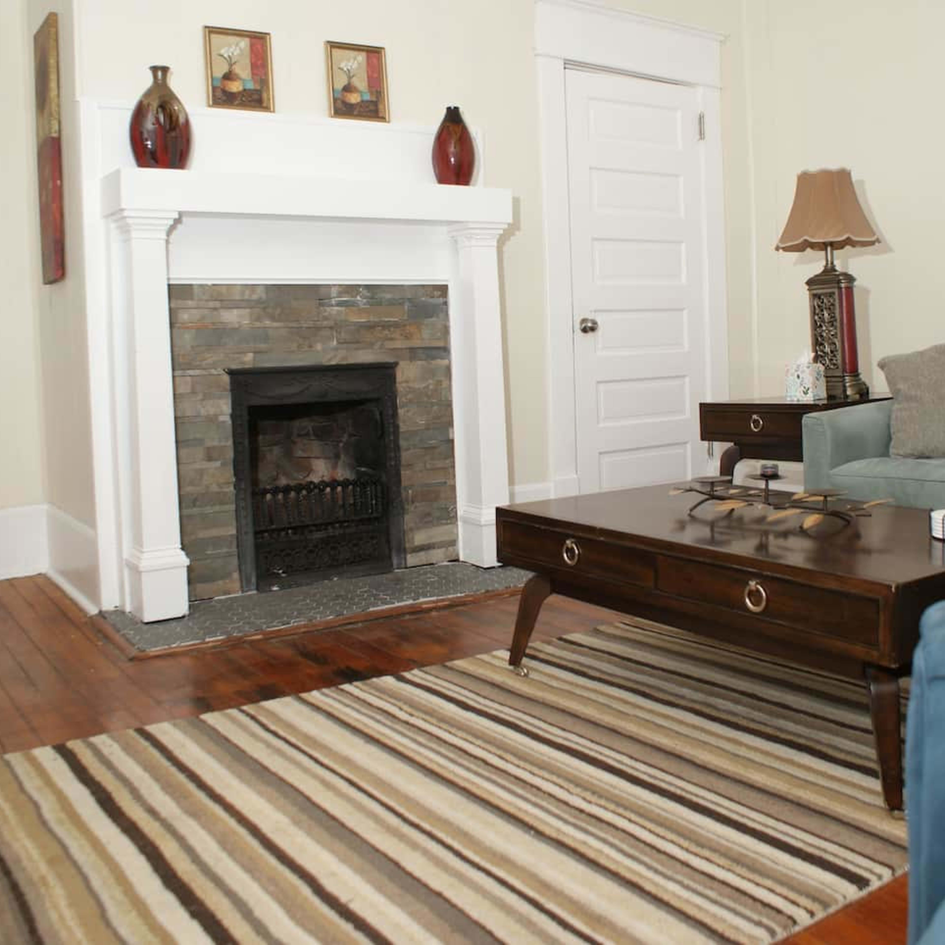 A living room with a stone fireplace, a wooden coffee table, and a blue sofa, all arranged on a striped rug.