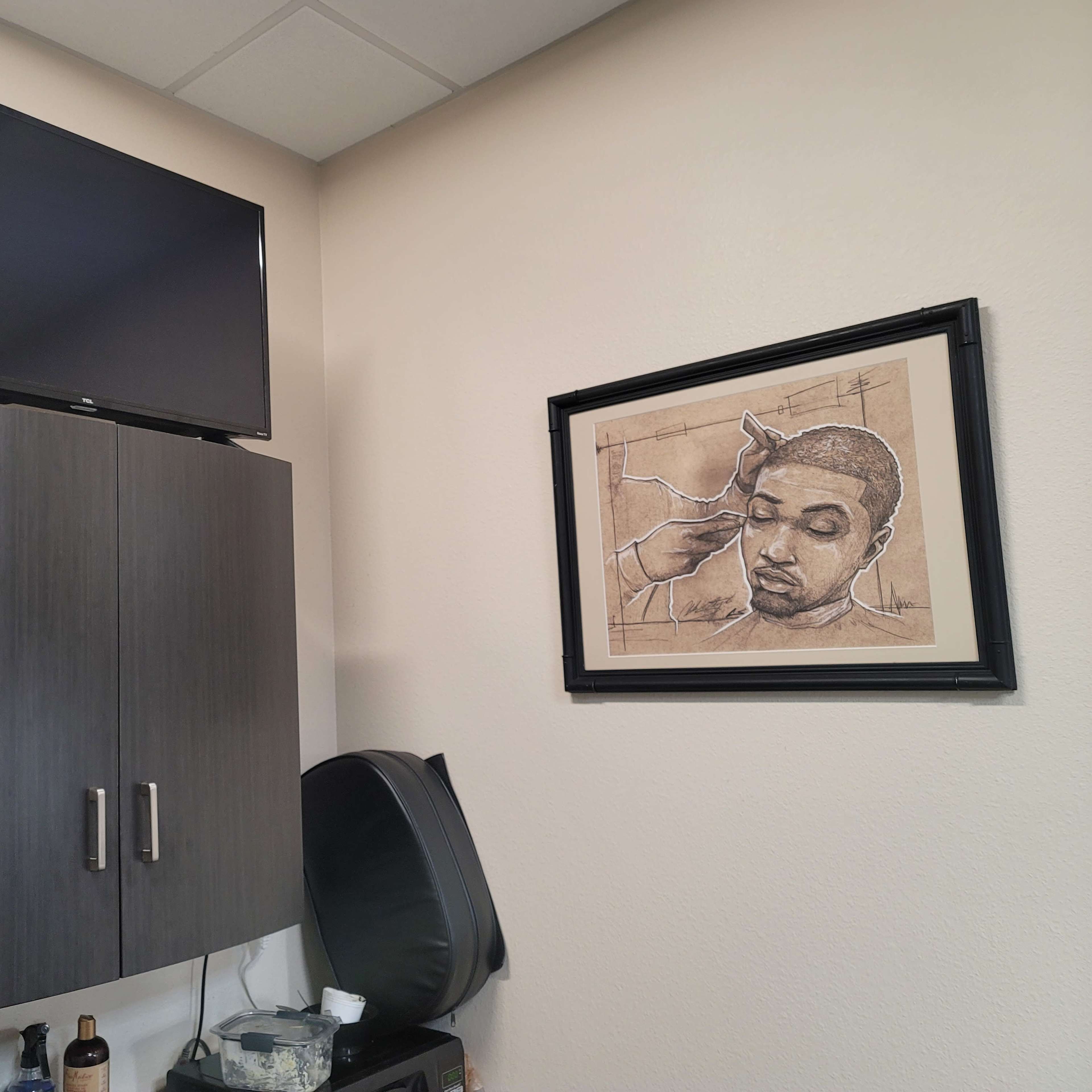 A wall with a mounted television, a framed artwork of a person getting a haircut, and a dark cabinet beneath them.