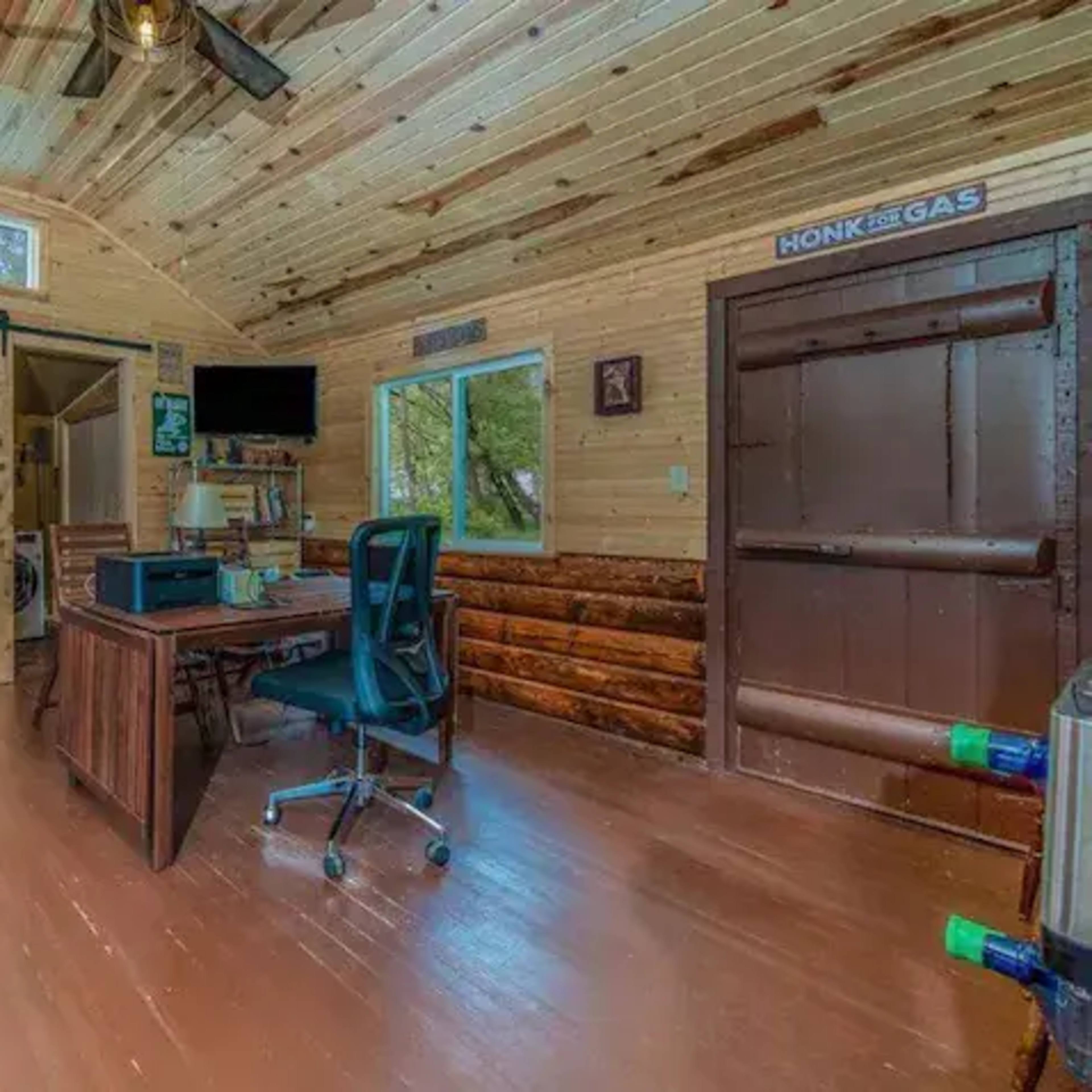 A small wooden cabin interior with a desk, chair, red cabinets, and a door leading outside.