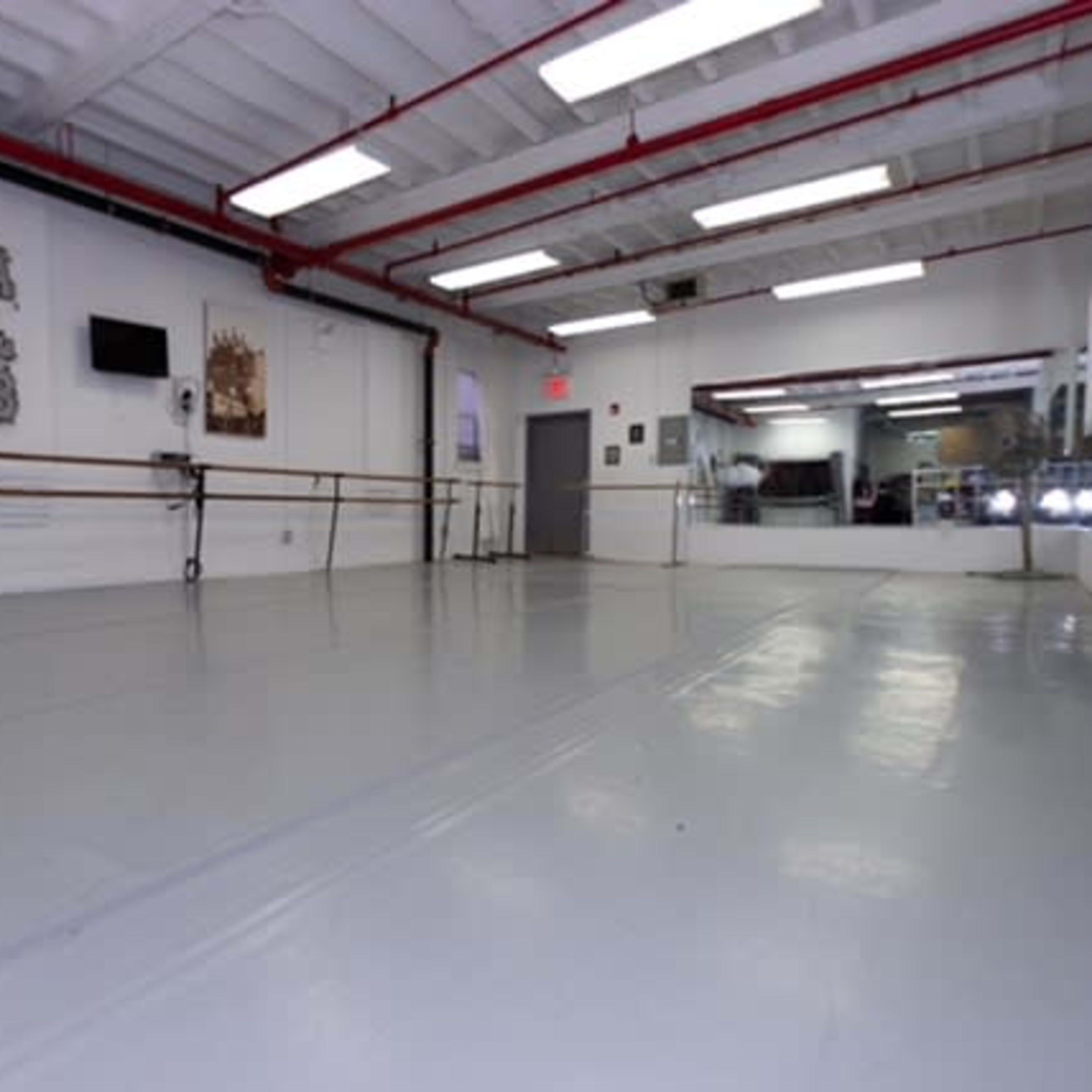A spacious dance studio featuring a mirrored wall, ballet barres, and a polished gray floor.