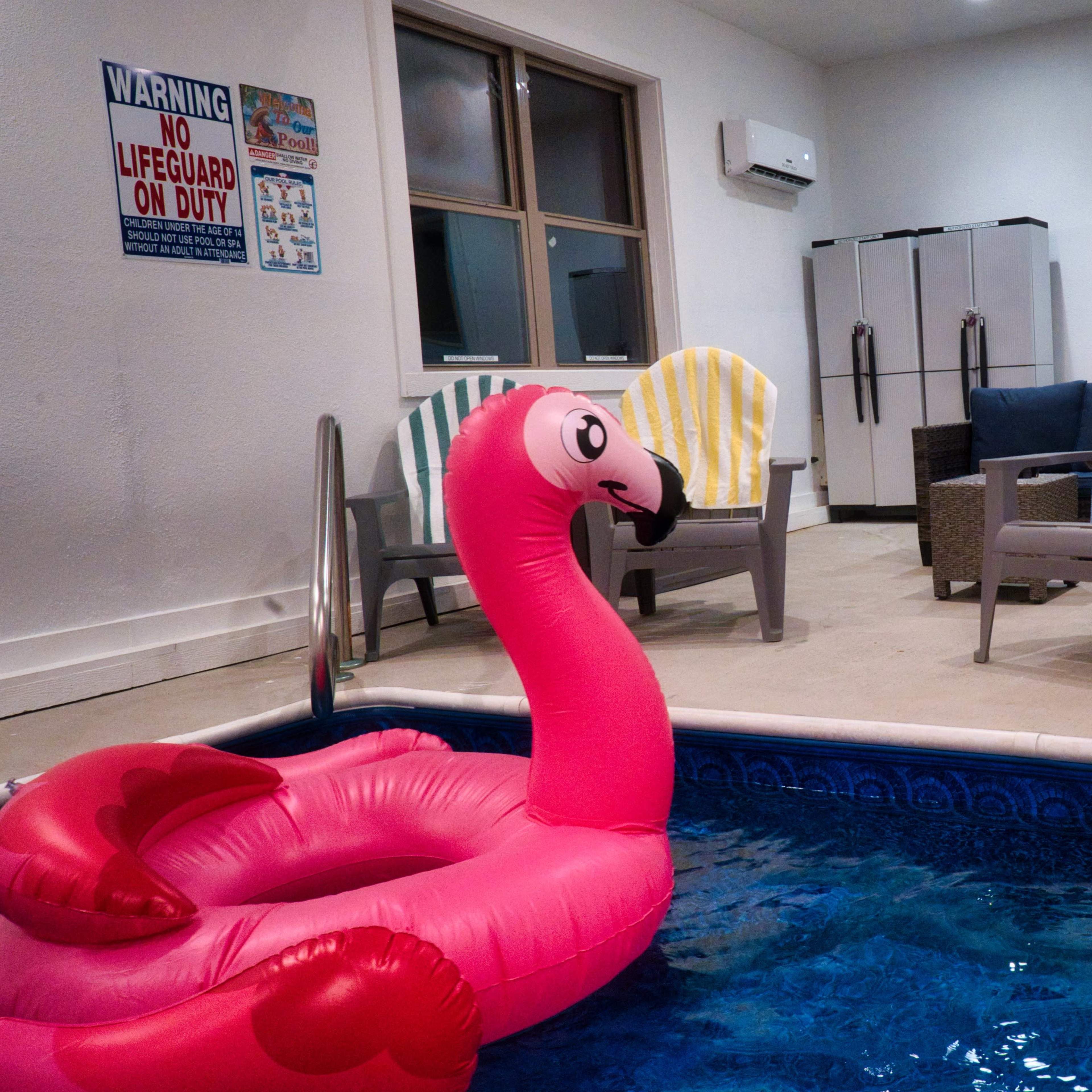 An indoor space featuring a small pool with a pink flamingo float, surrounded by colorful deck chairs and a set of refrigerators in the background.