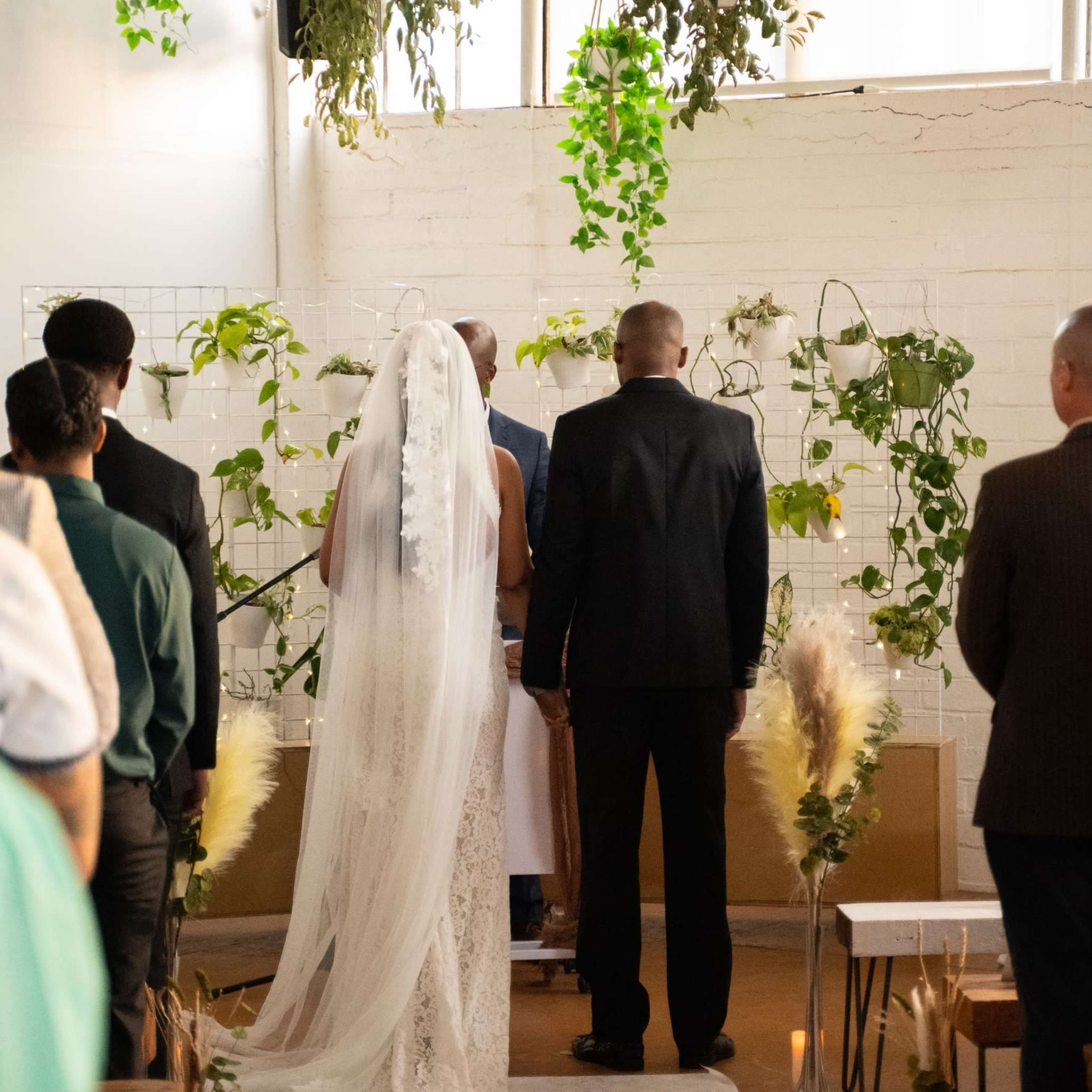 A couple stands at the altar surrounded by greenery, while guests look on during a wedding ceremony.