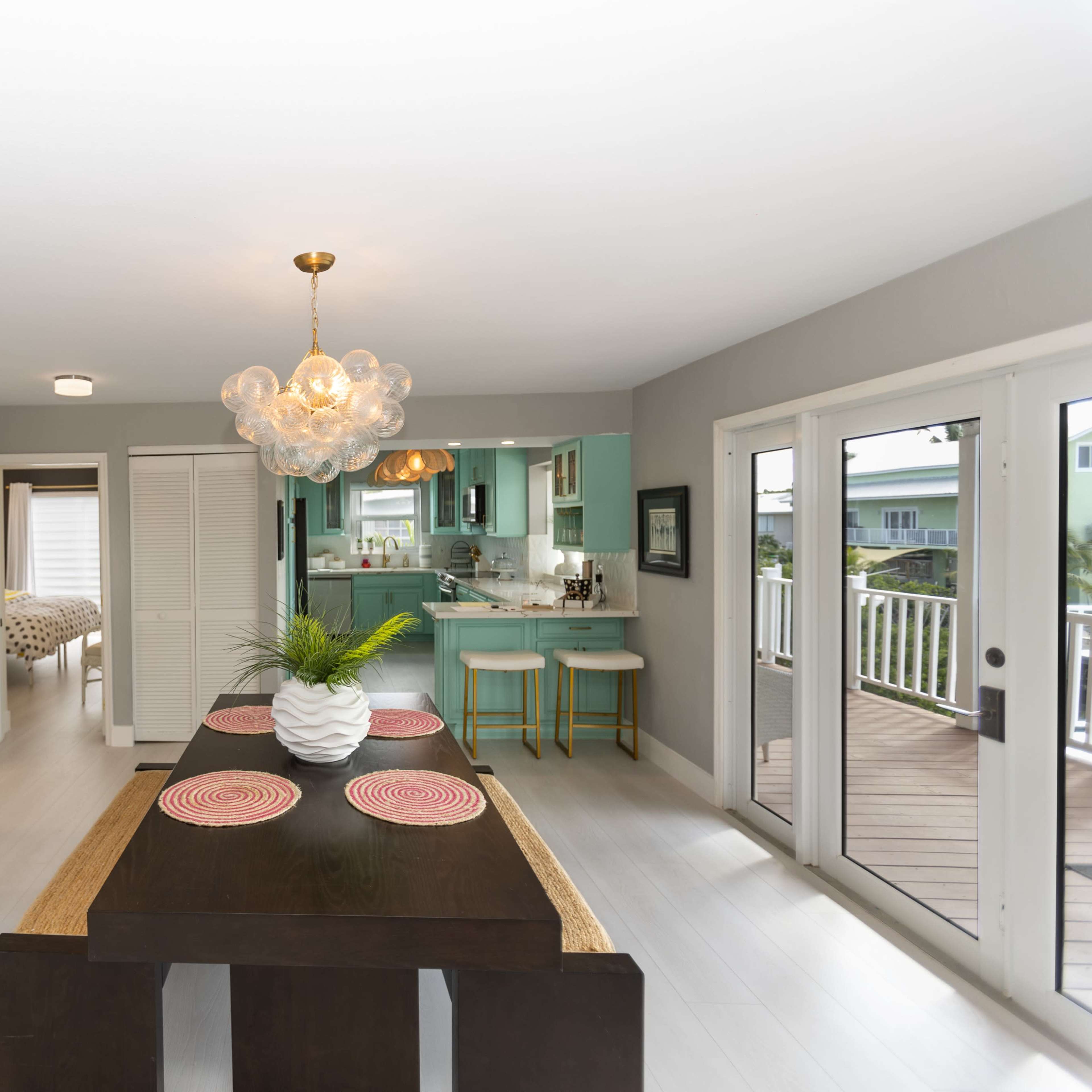 A modern dining area with a dark wooden table, a round light fixture, and a green kitchen visible in the background.