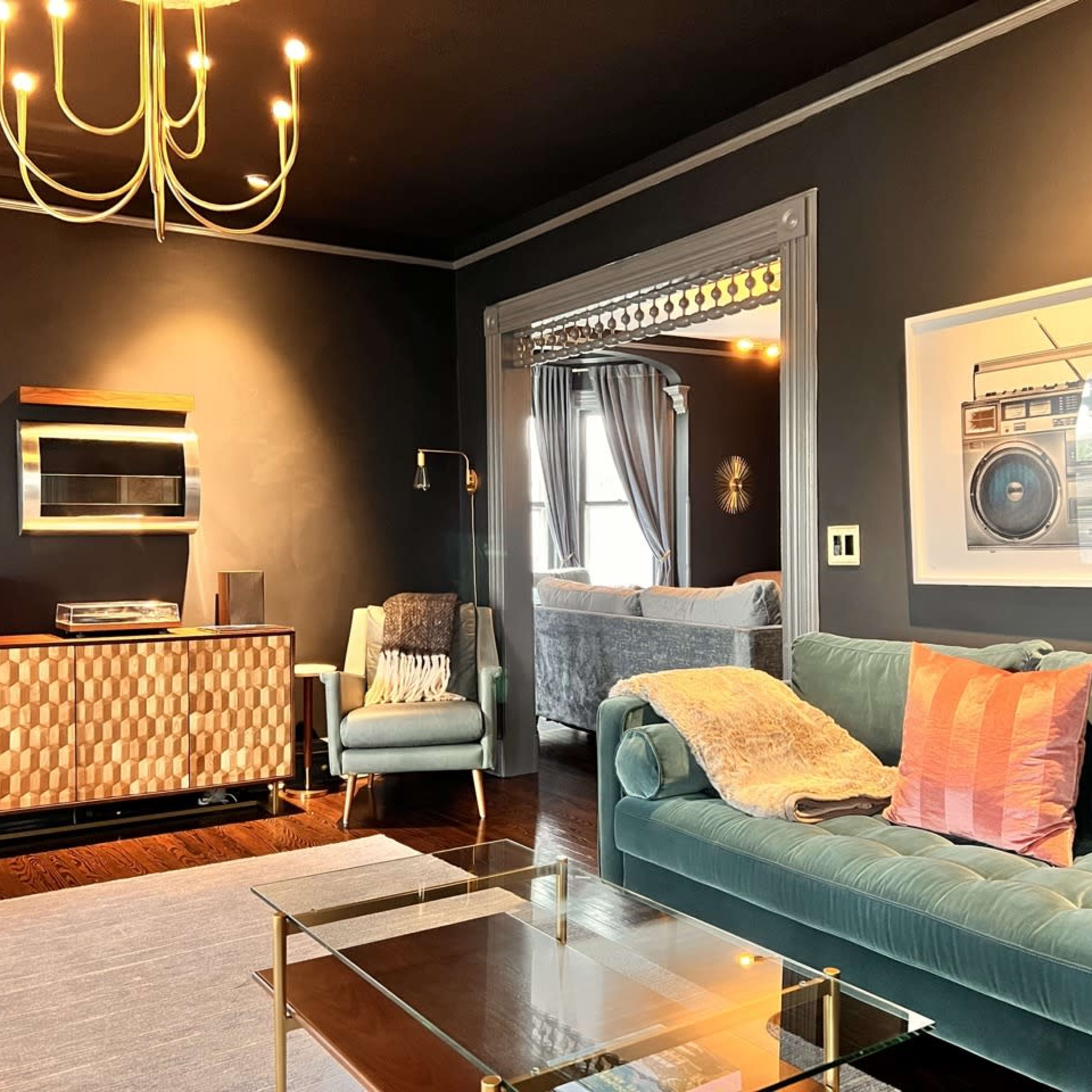 A modern living room featuring a teal sofa, a glass coffee table, and a wall decorated with an art piece of a vintage boombox.