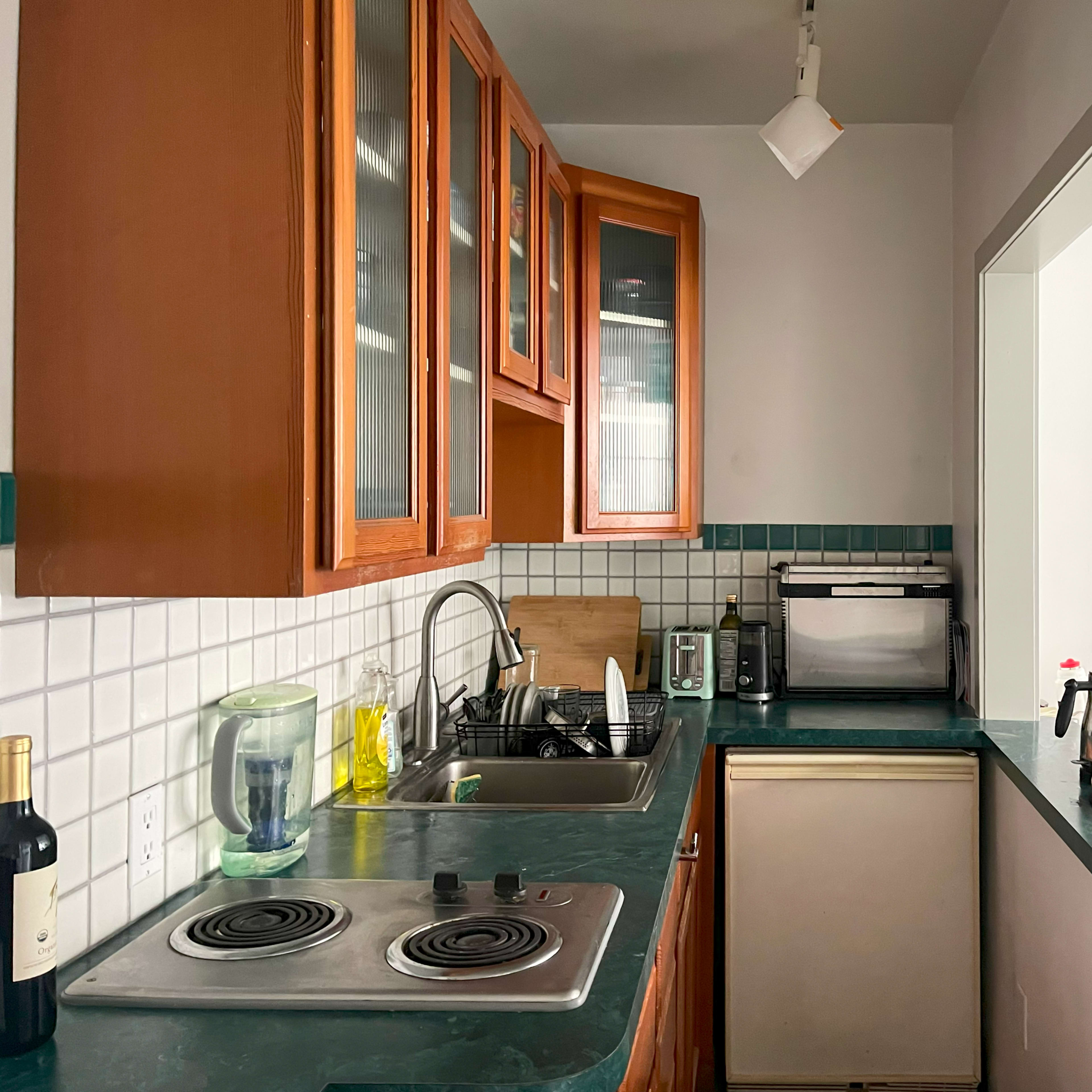 A kitchen with wooden cabinets, a green countertop, a sink, a stove, and various kitchen appliances.