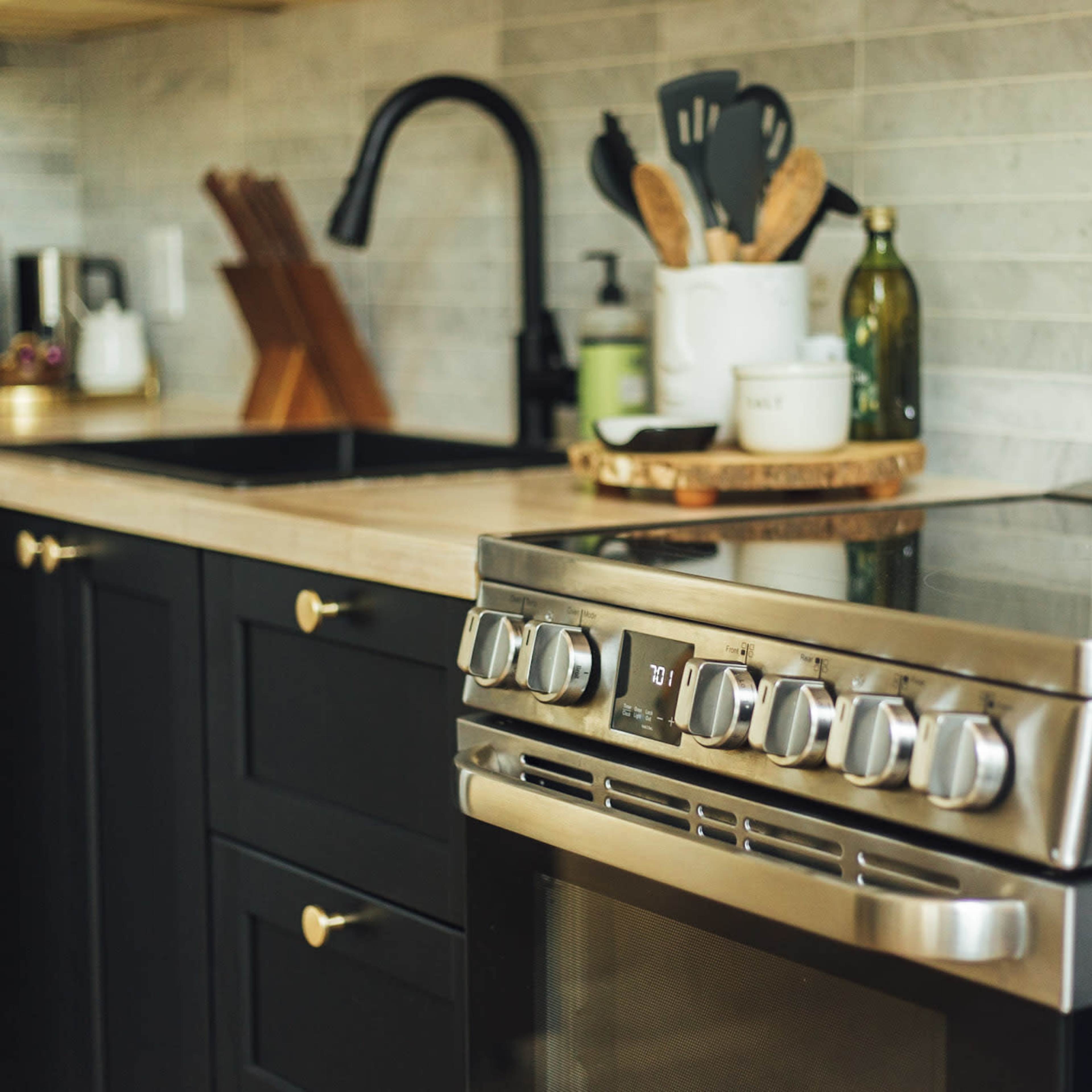 A modern kitchen with black cabinets, a stainless steel stove, and a countertop with utensils and various kitchen items.