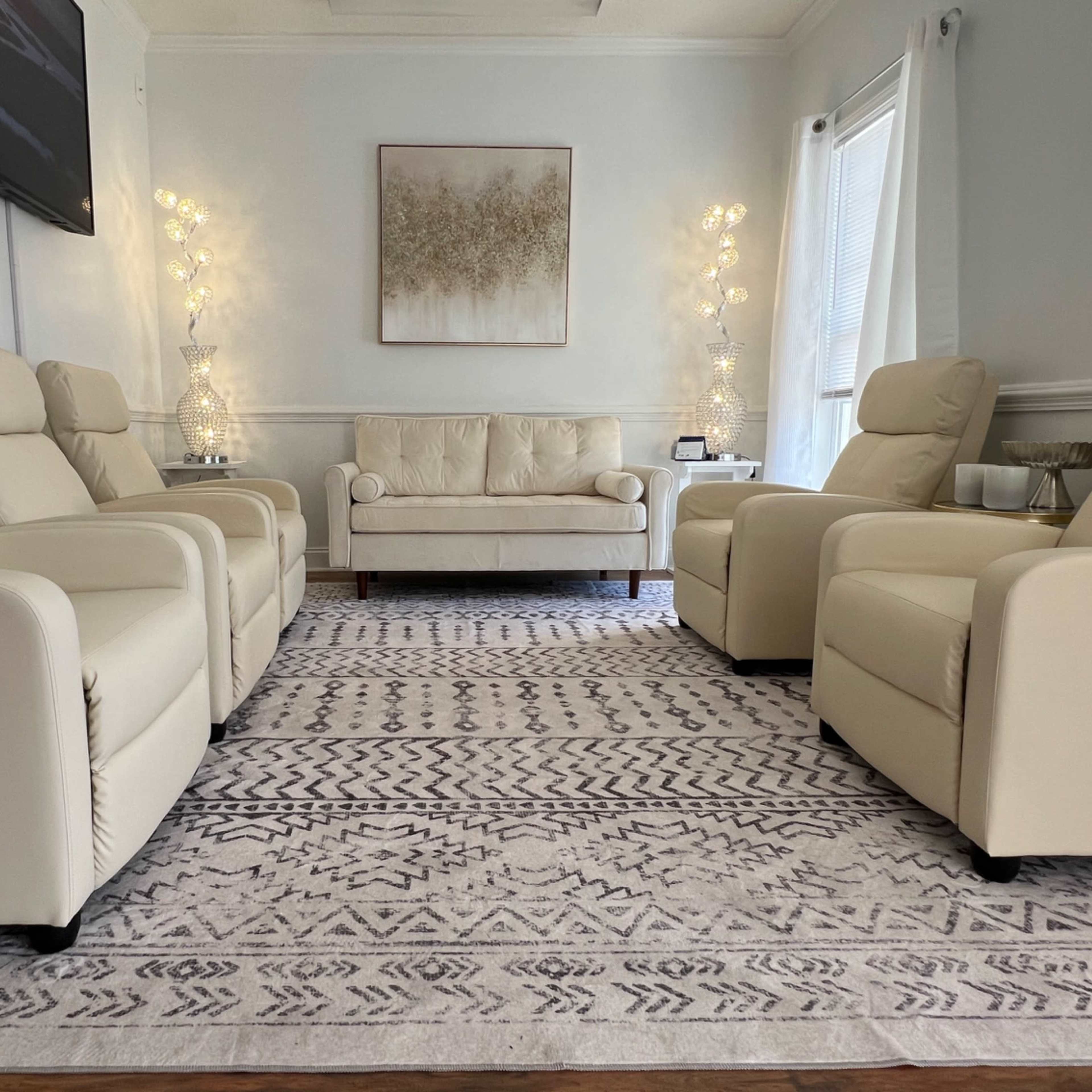 A neatly arranged living room with cream-colored recliner chairs, a sofa, and a decorative rug.