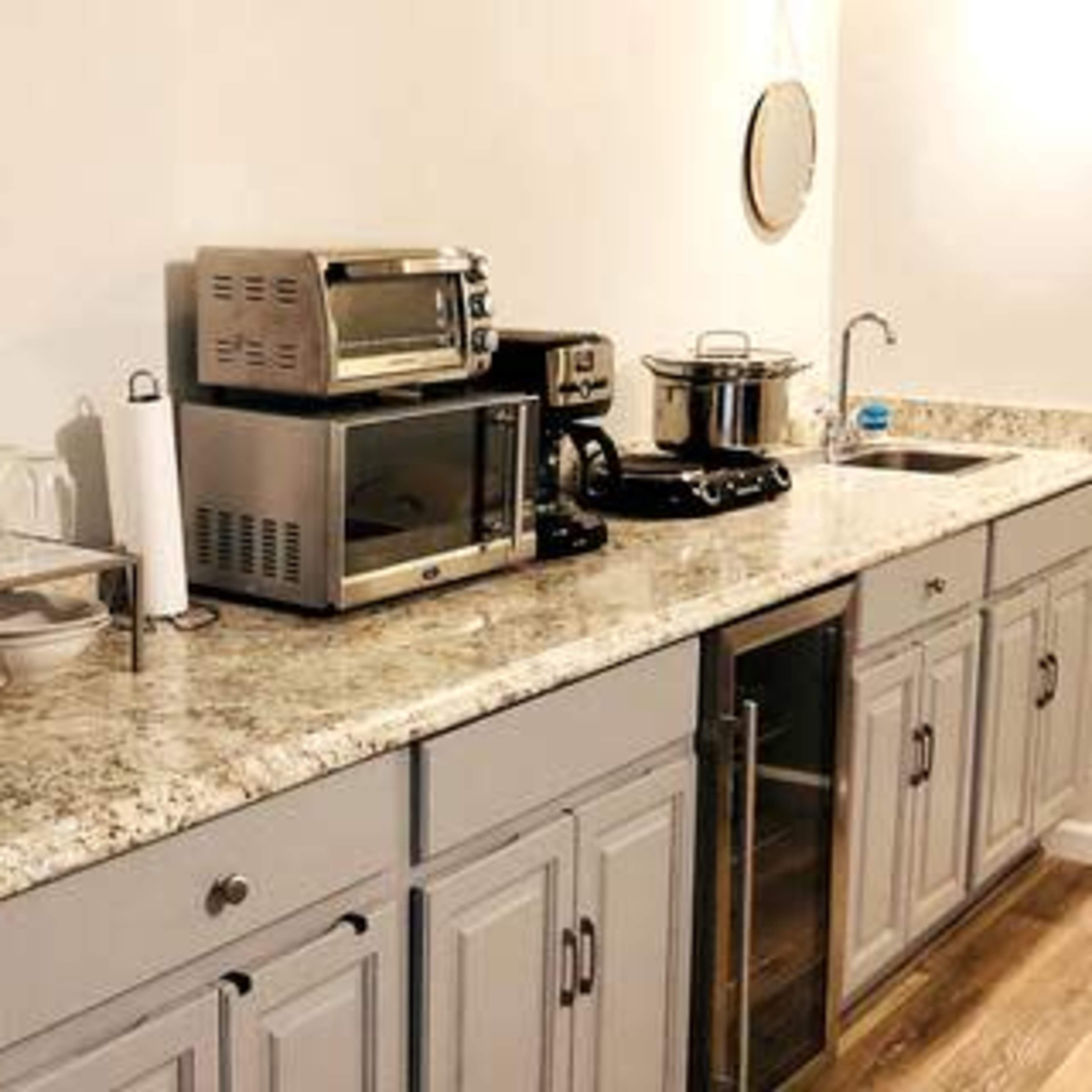 A kitchen countertop with a microwave, toaster oven, coffee maker, and sink, along with plates and glassware on a metal rack.
