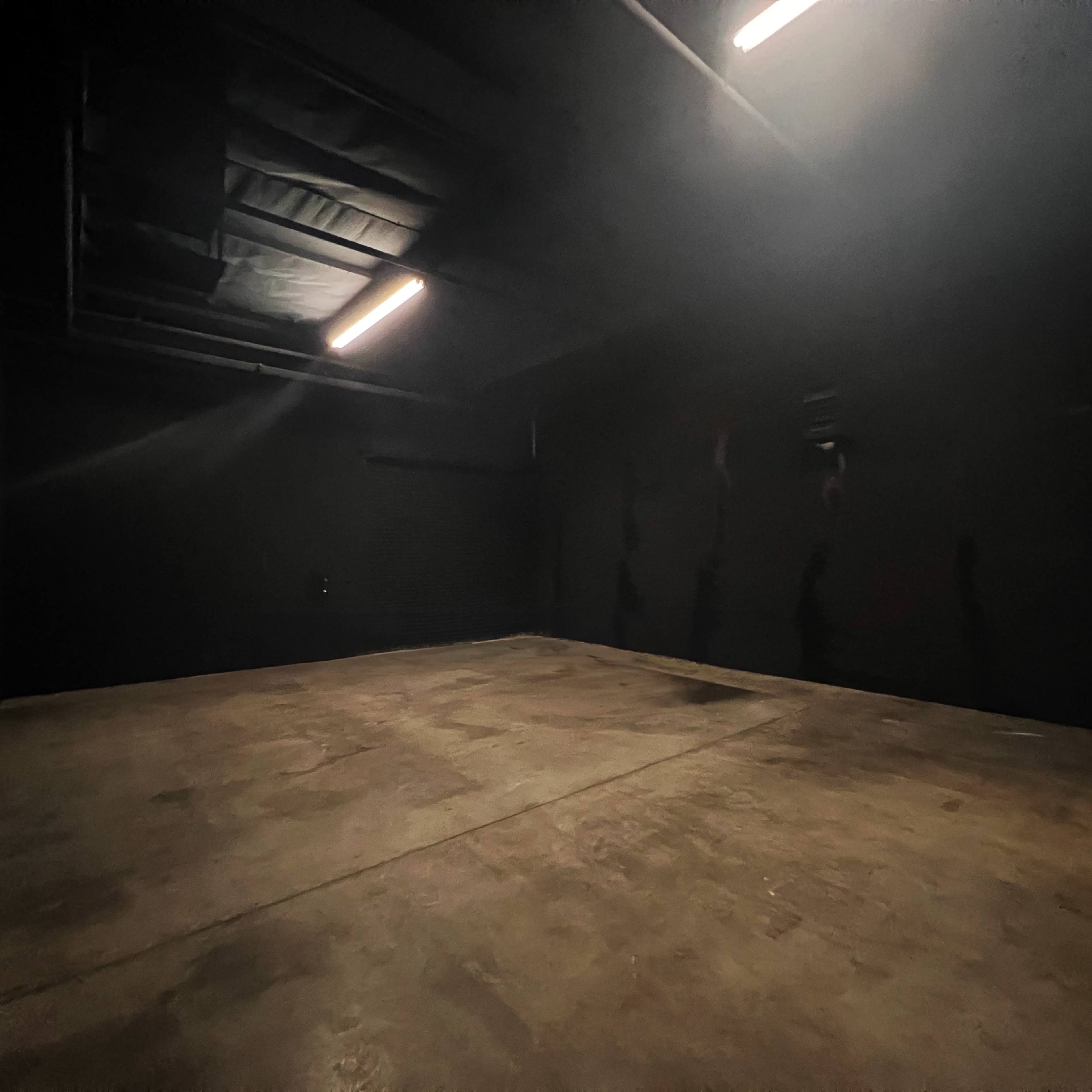 A dimly lit, empty room with dark walls and a concrete floor.