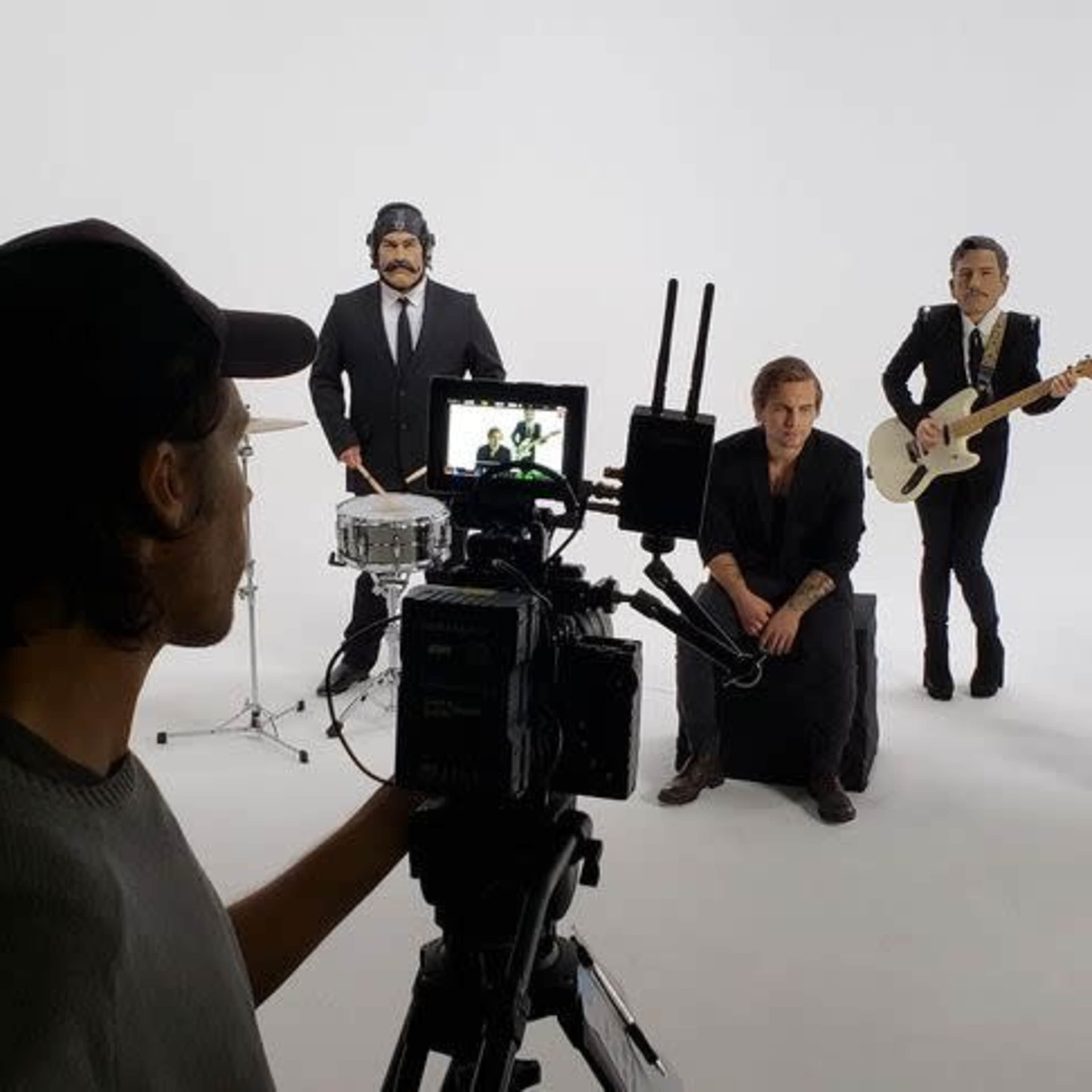 A film crew captures a band performing in a studio with a white backdrop and a heart-shaped decoration.