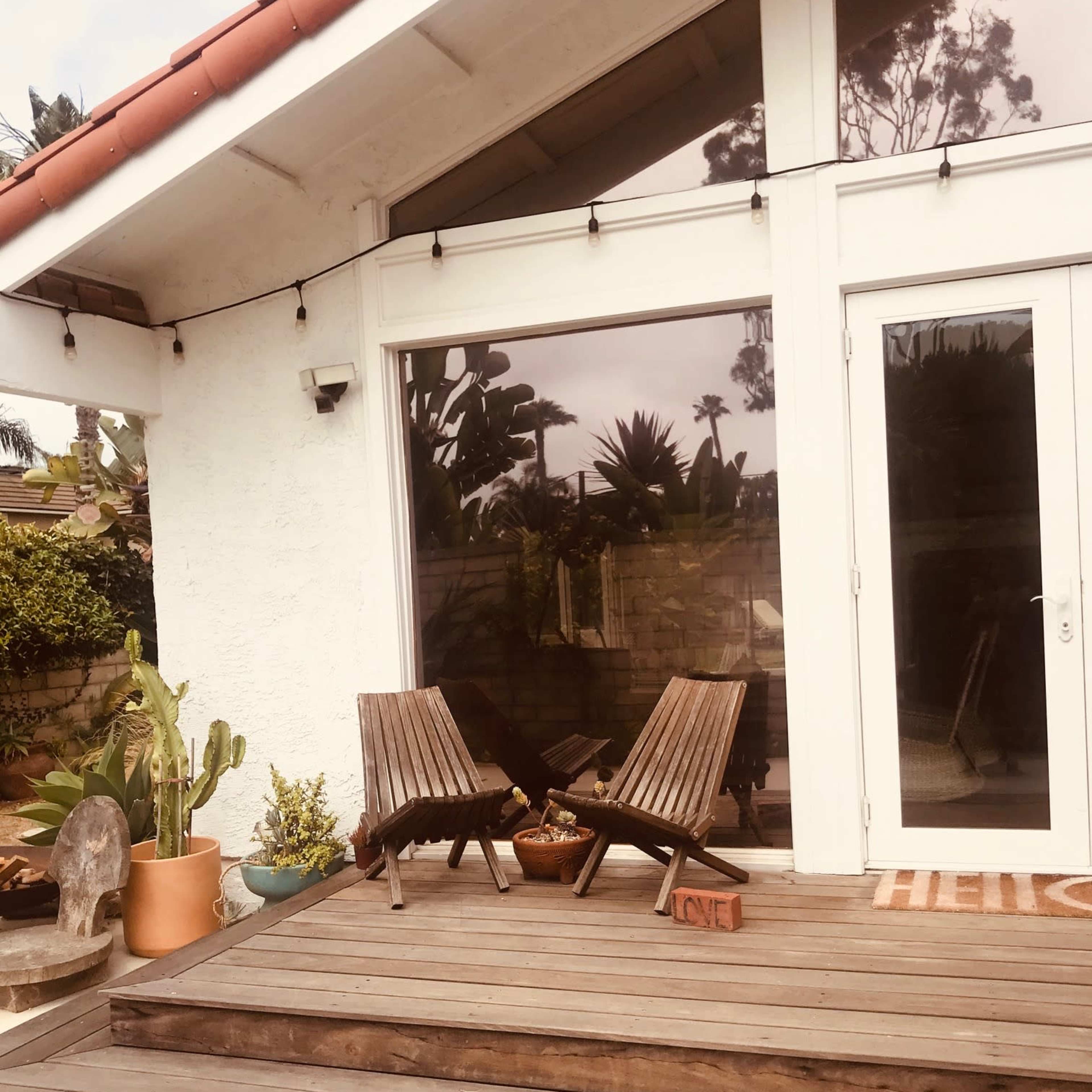 A pair of wooden lounge chairs sits on a wooden deck in front of a large glass sliding door.