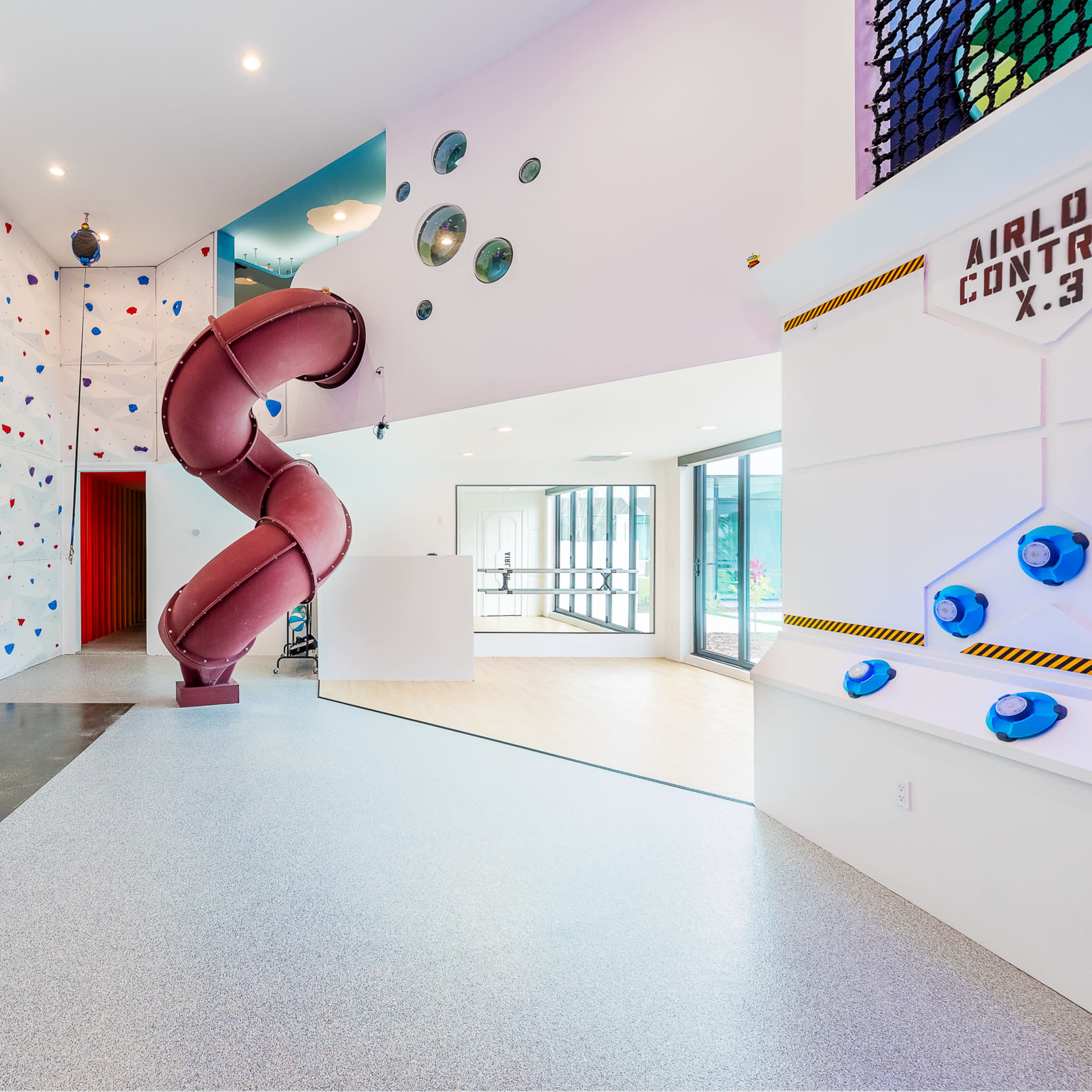 A modern recreational space featuring a climbing wall, a basketball hoop, and a spiral slide.