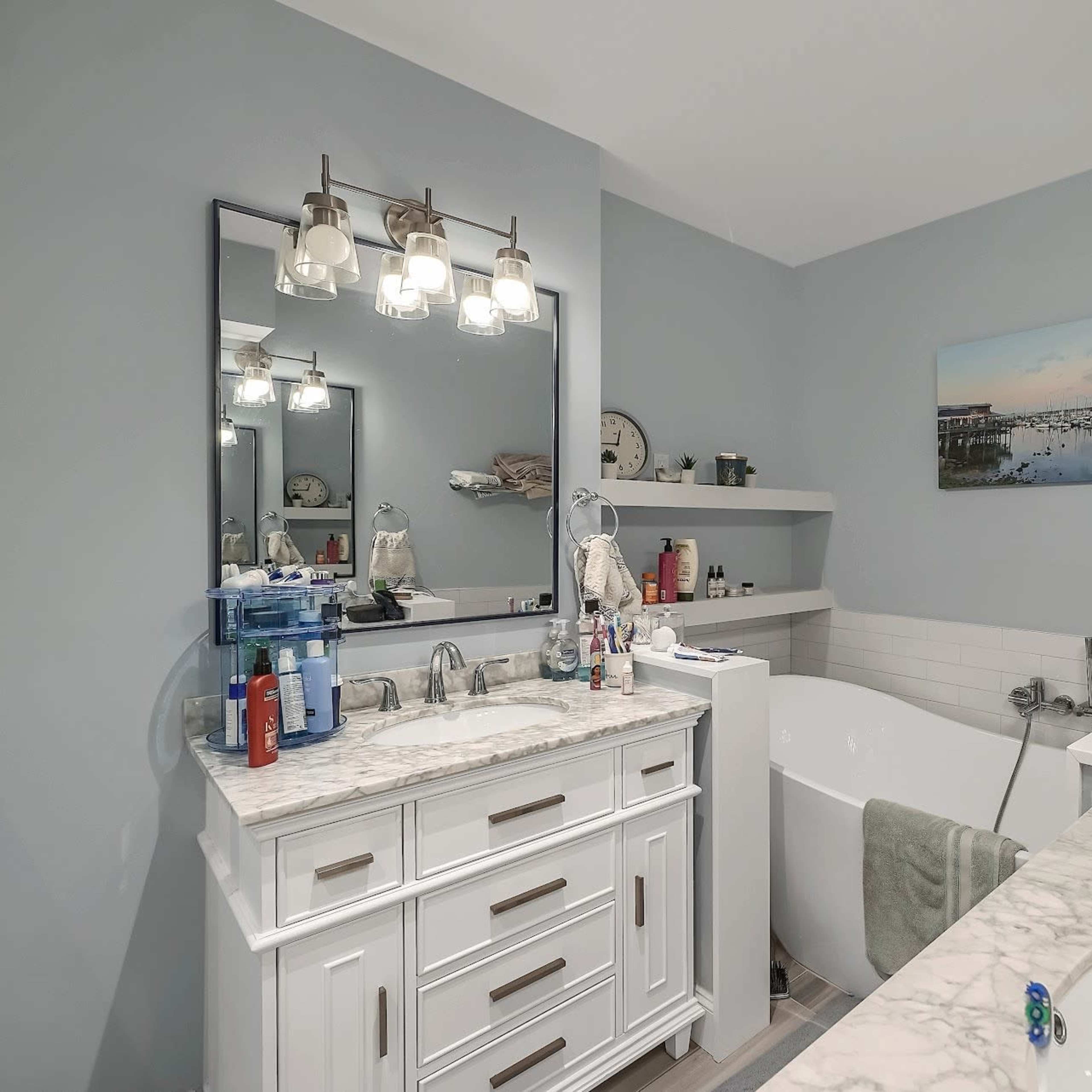 A modern bathroom featuring a white double vanity with a marble countertop, a freestanding bathtub, and light gray walls.