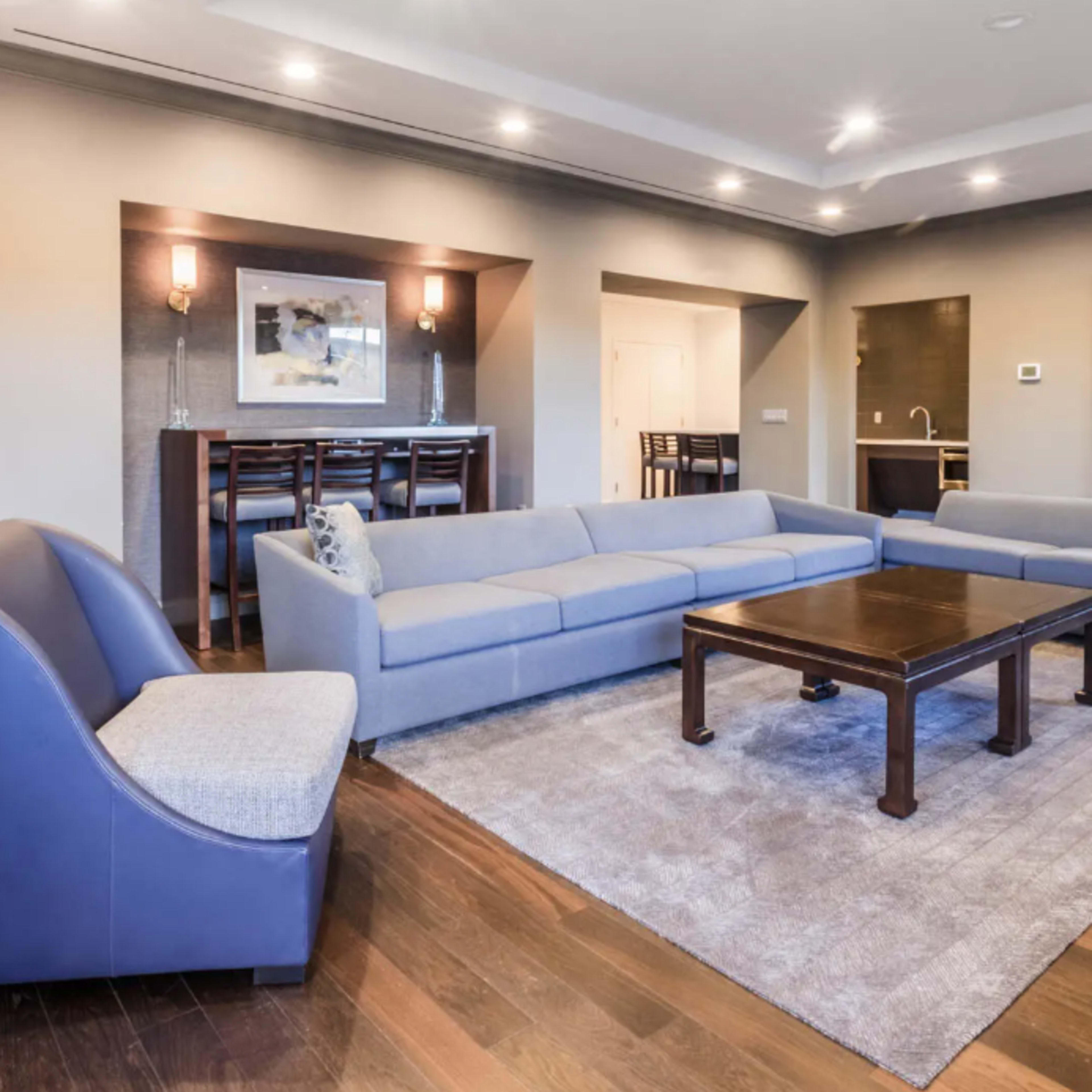 A modern living room with a sectional sofa, a wooden coffee table, and a bar area in the background.