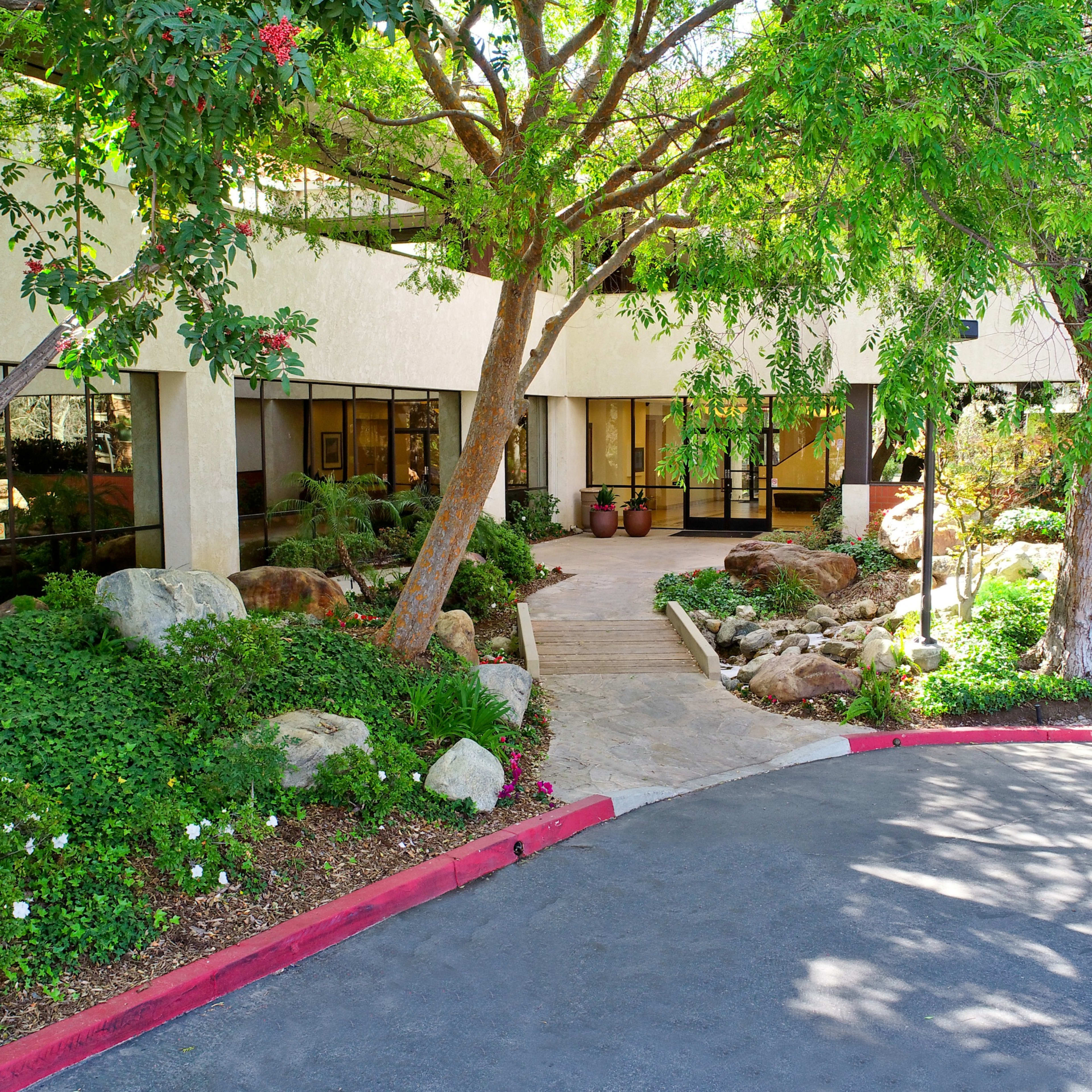 An entrance to a building surrounded by landscaped greenery, rocks, and trees.