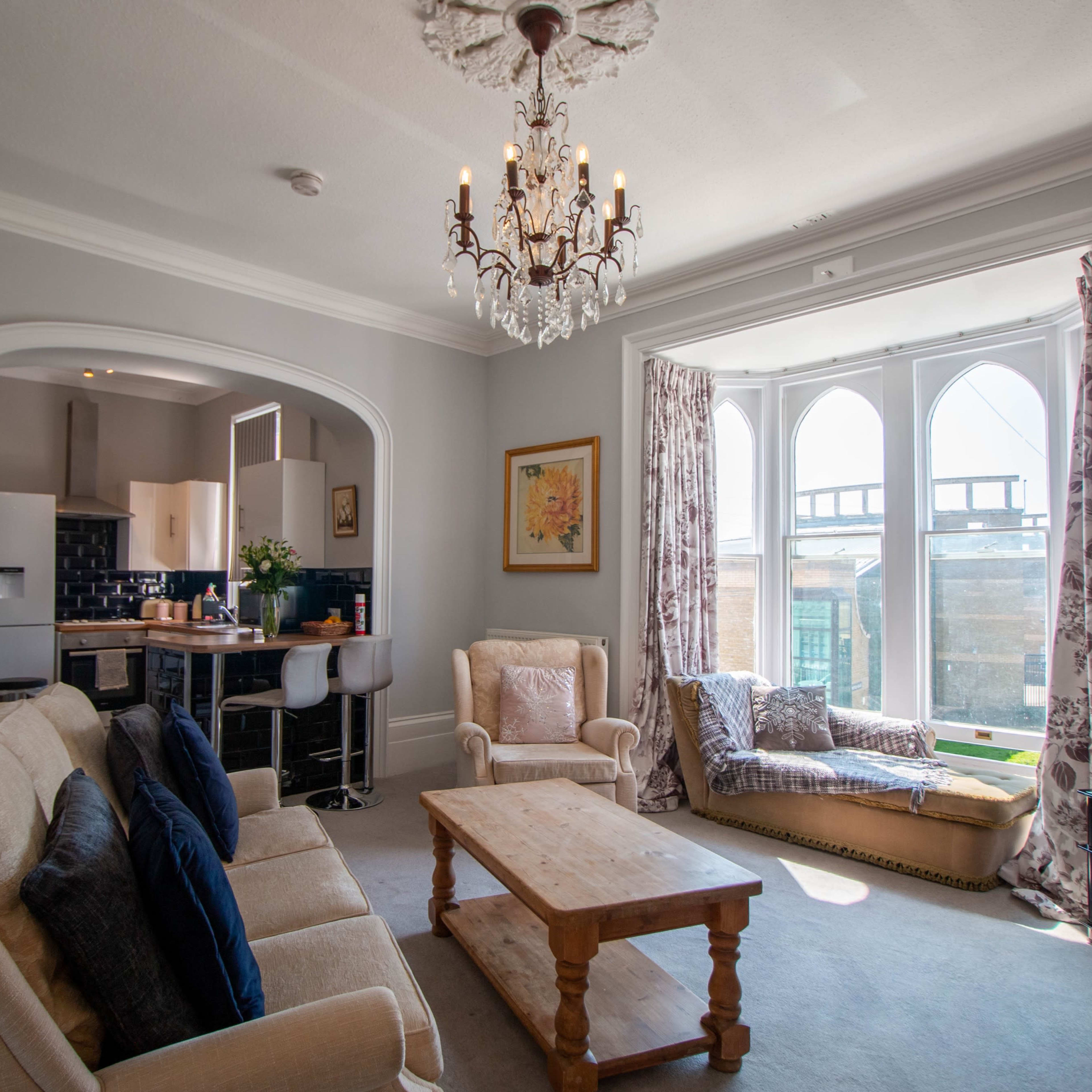 A living room with a beige sofa, a wooden coffee table, and a bay window featuring a window seat adorned with cushions.