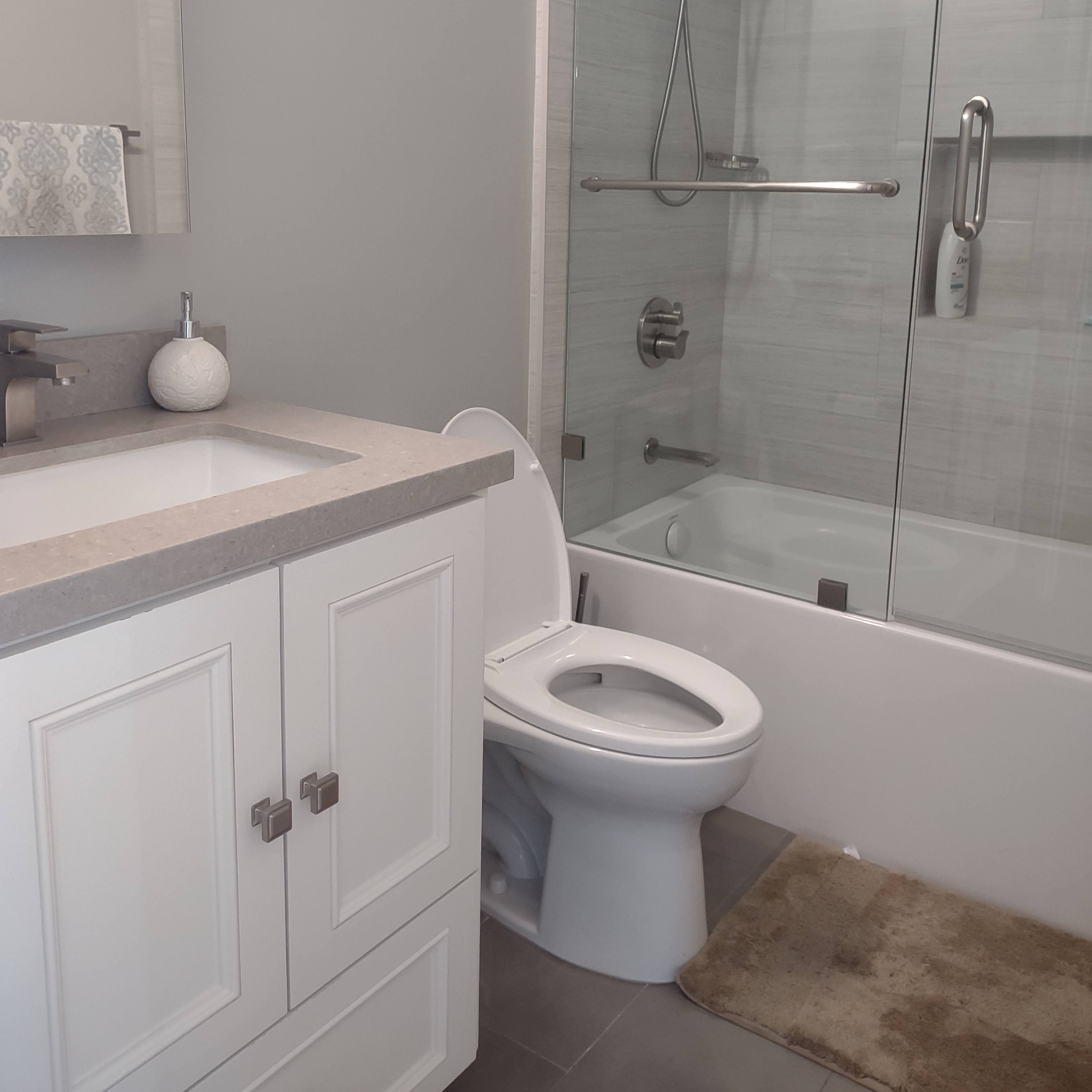 A modern bathroom with a glass shower enclosure, a toilet, a sink with a countertop, and light-colored walls.