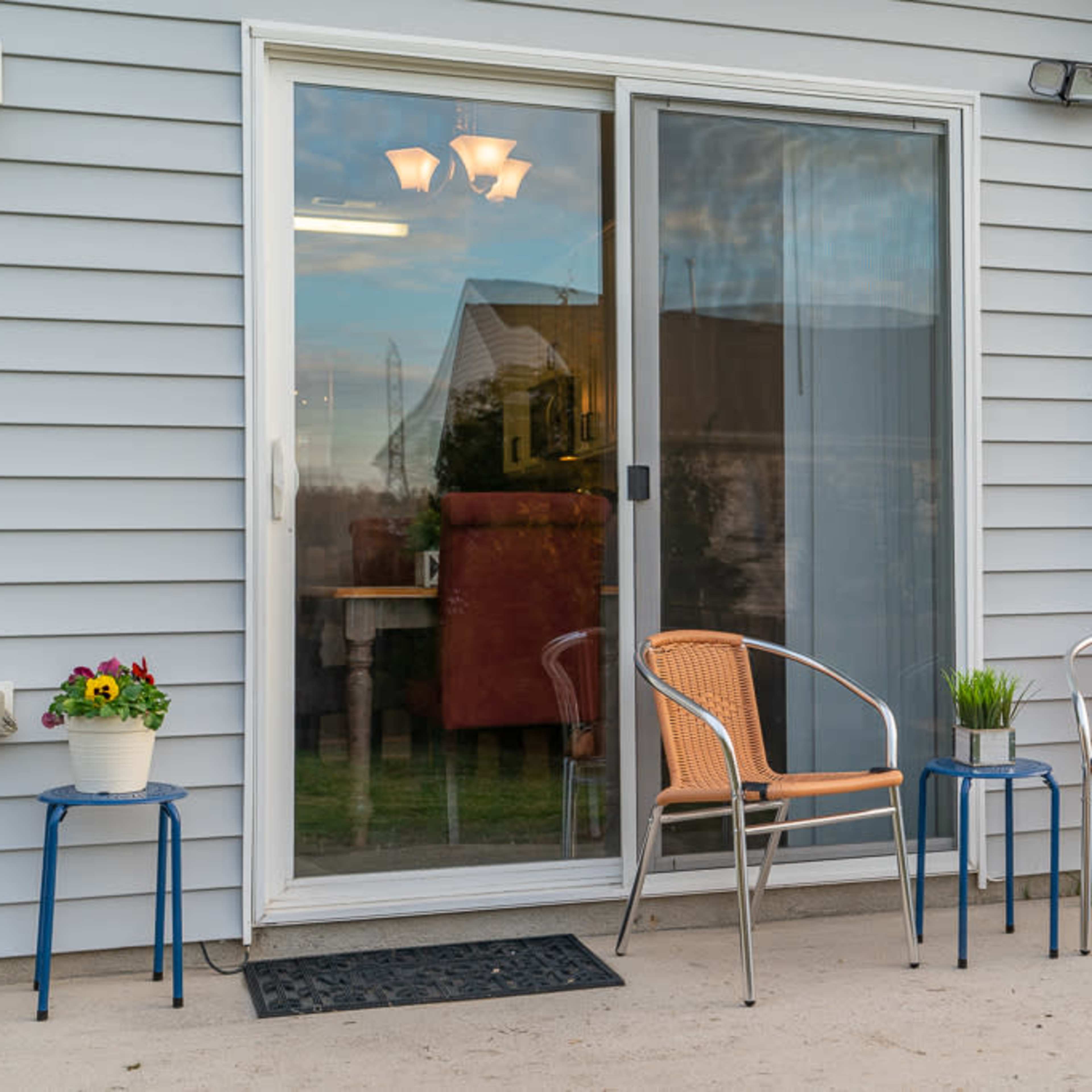 A patio with two chairs and two small tables arranged in front of a sliding glass door.