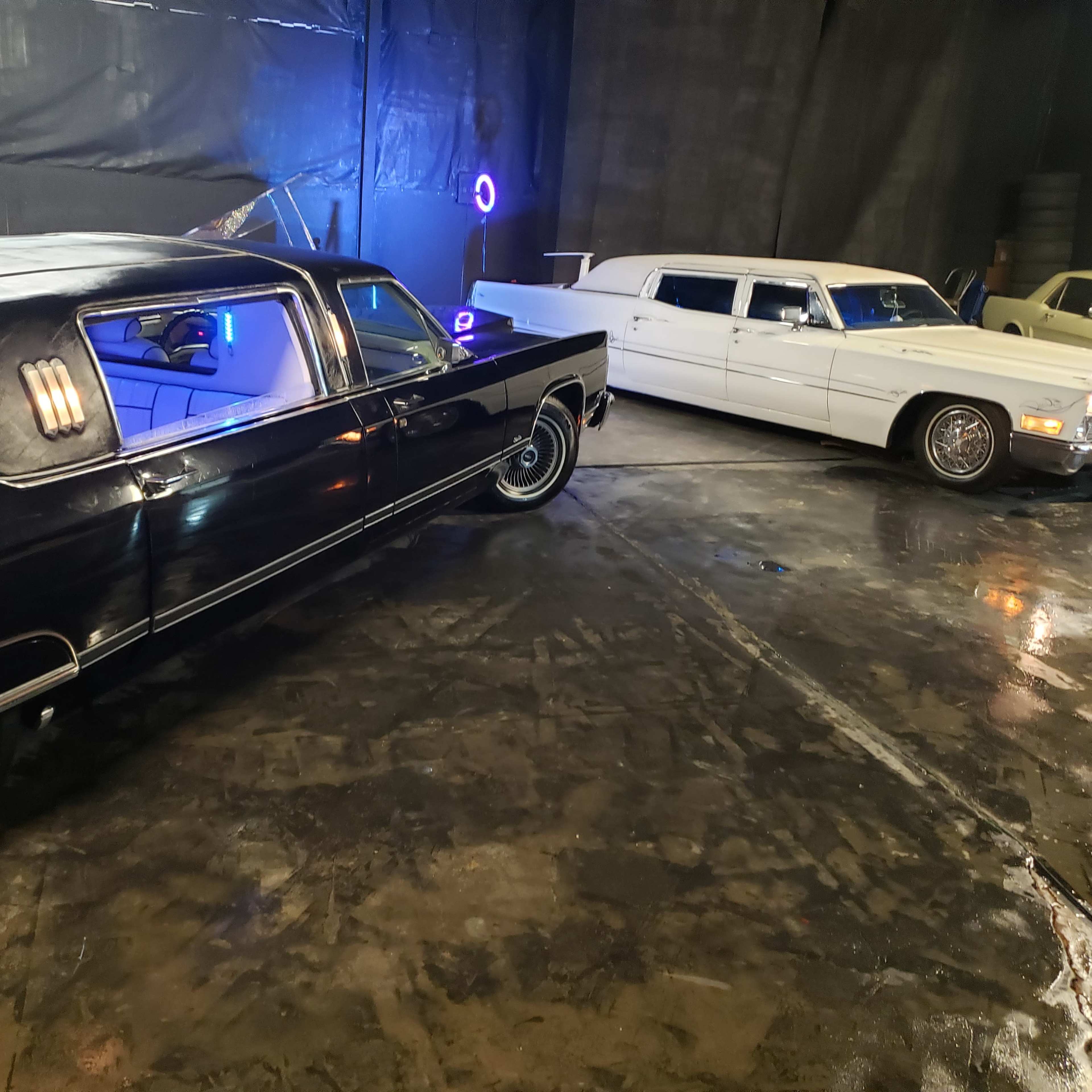 A black hearse and a white limousine parked on a shiny floor in a dimly lit space.