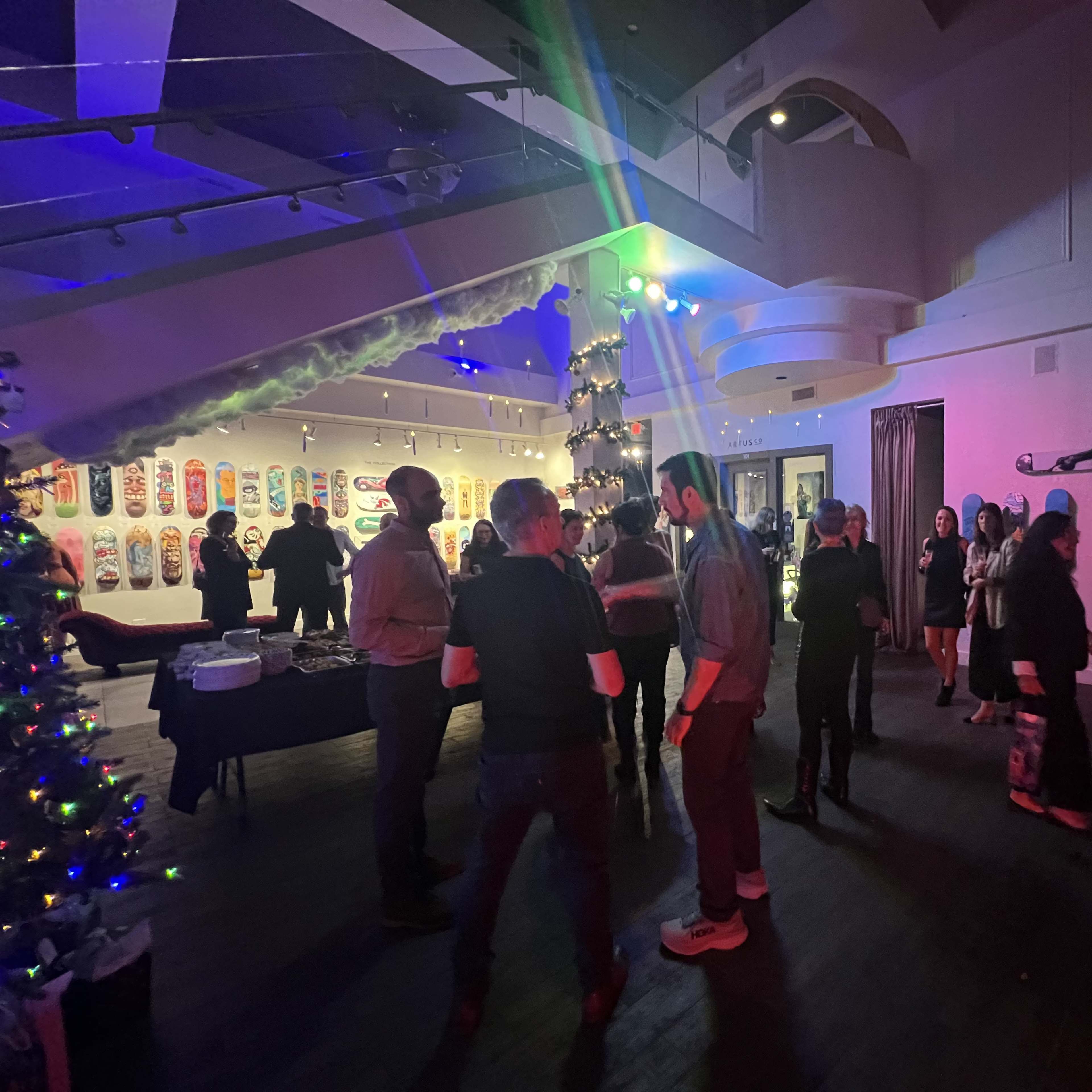 A group of people socializes inside a venue decorated with skateboard art and a Christmas tree.