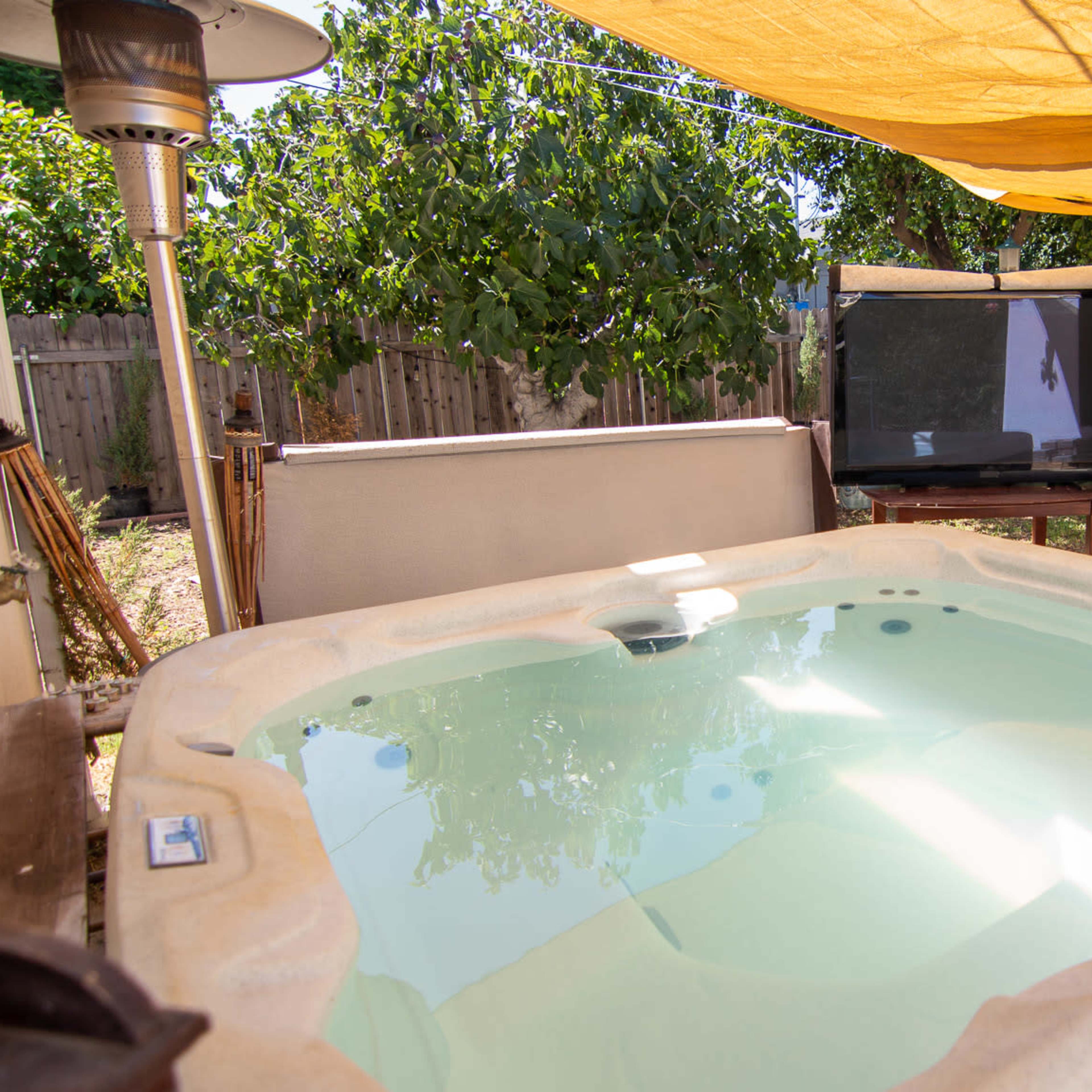 A hot tub under a yellow canopy in a backyard, with two large screens positioned nearby.