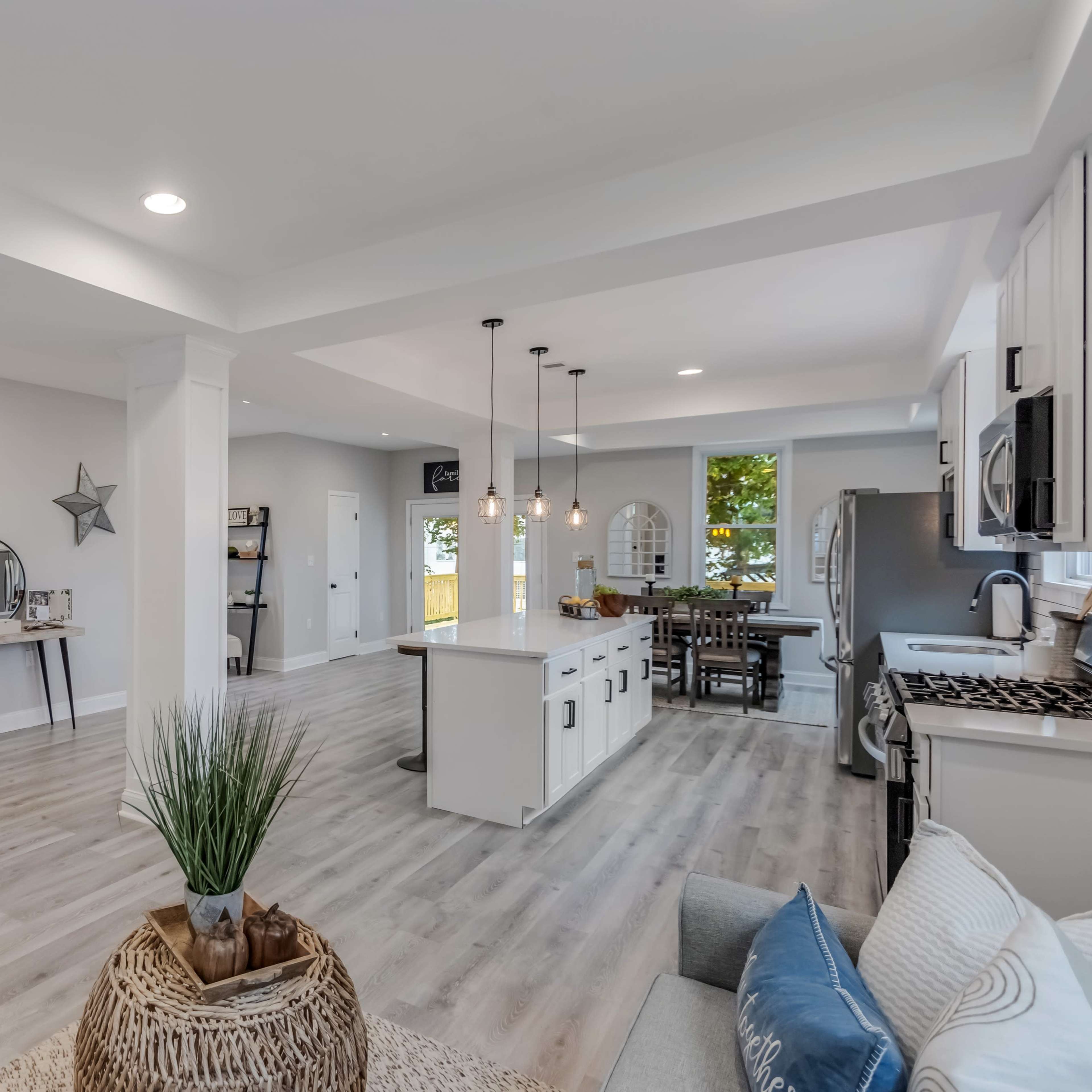 A spacious modern living area with an open kitchen and dining area, featuring light wood flooring and large windows allowing natural light.
