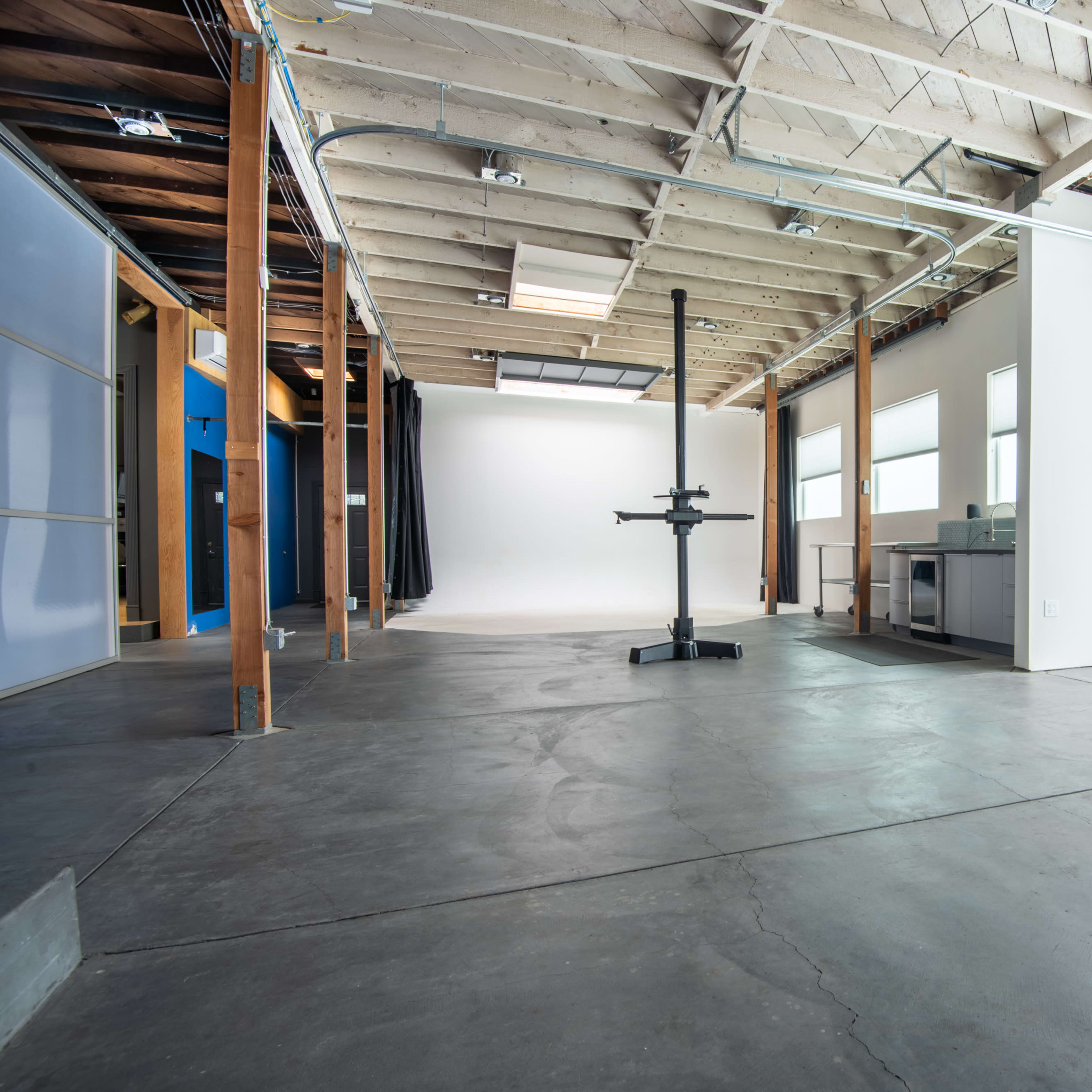 An empty studio space with concrete flooring, wooden beams, and a garage-style door.