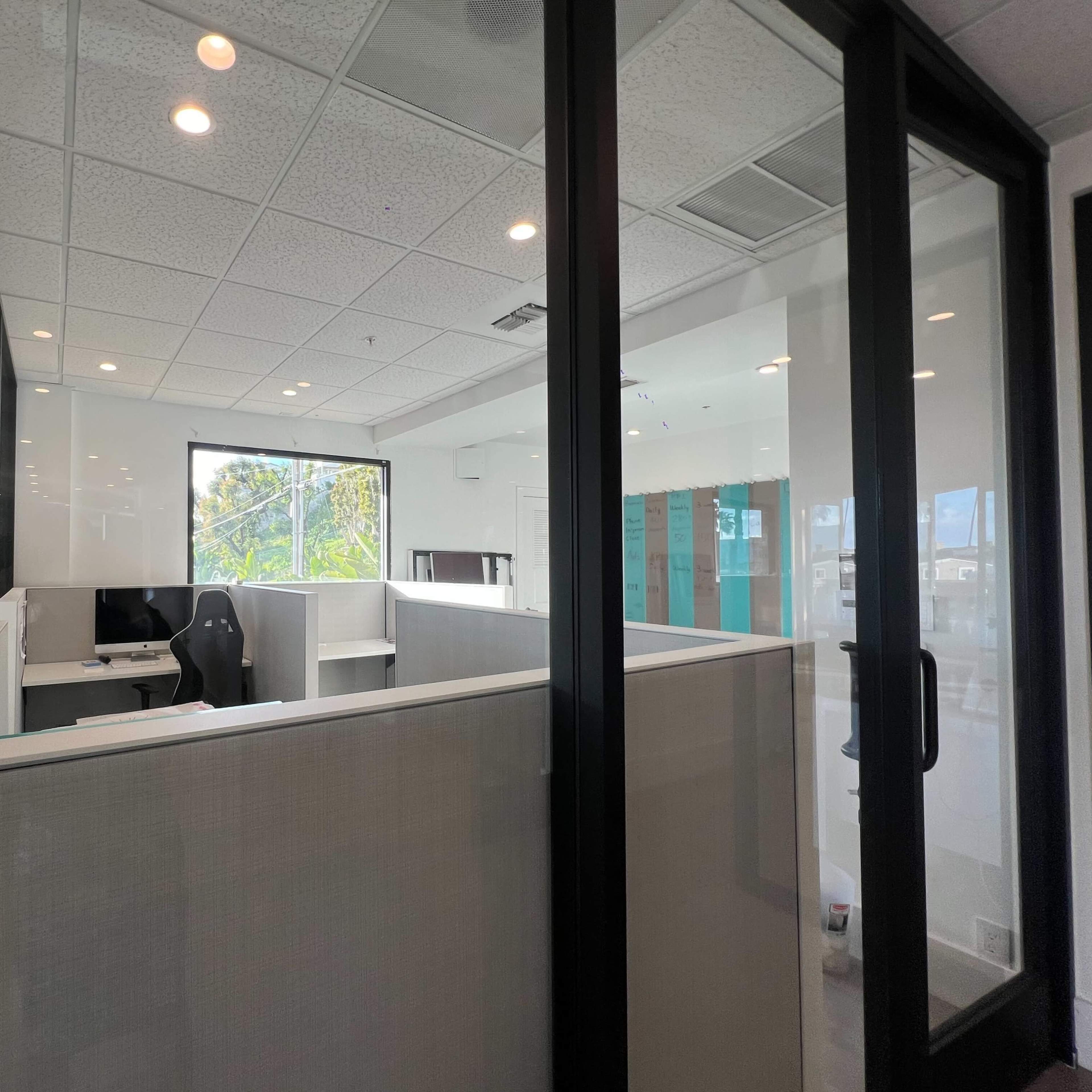 A modern office space with glass partitions, a desk with a computer, and a large window overlooking greenery.