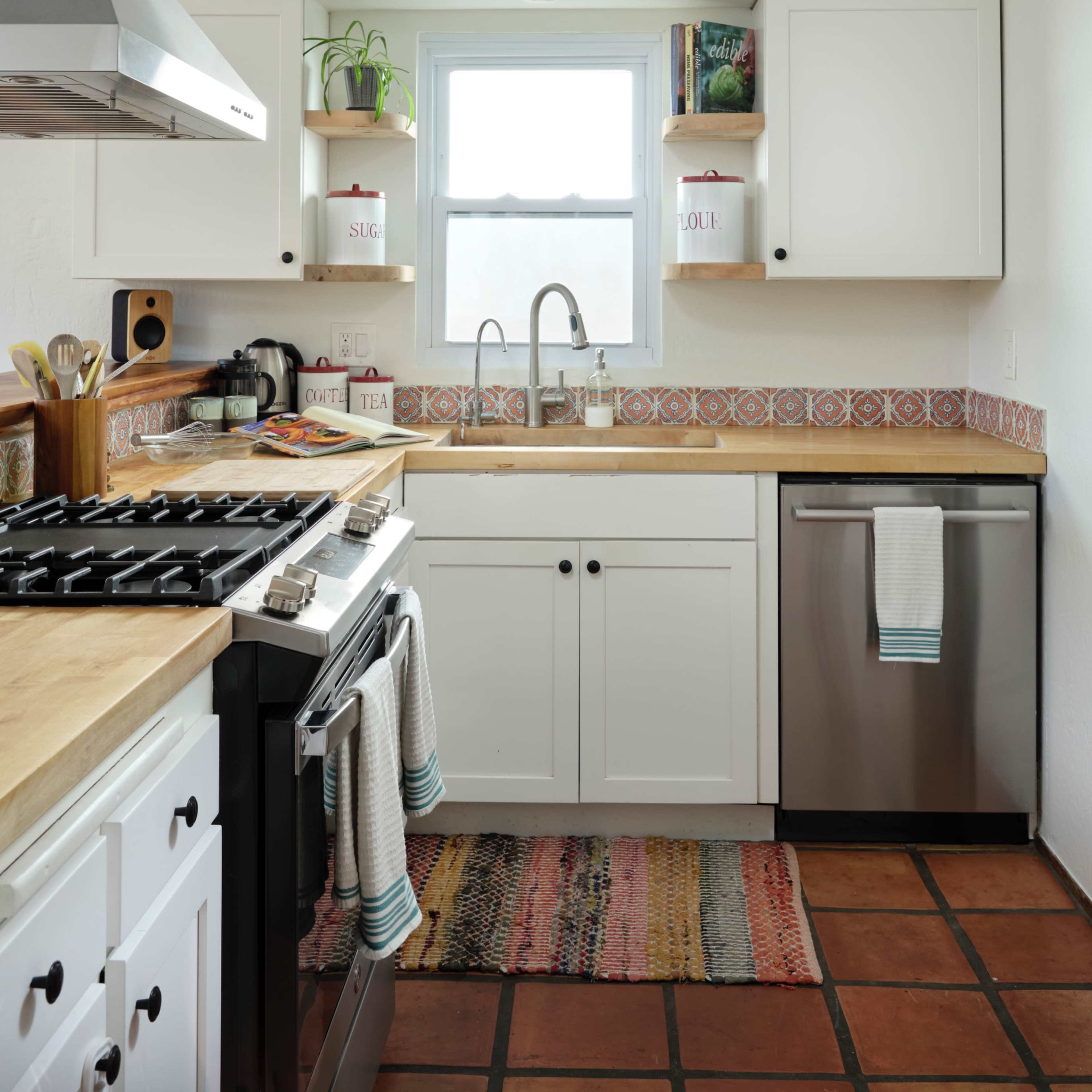The kitchen features white cabinetry, a stainless steel dishwasher, a gas stove, and a window above the sink with decorative shelves.