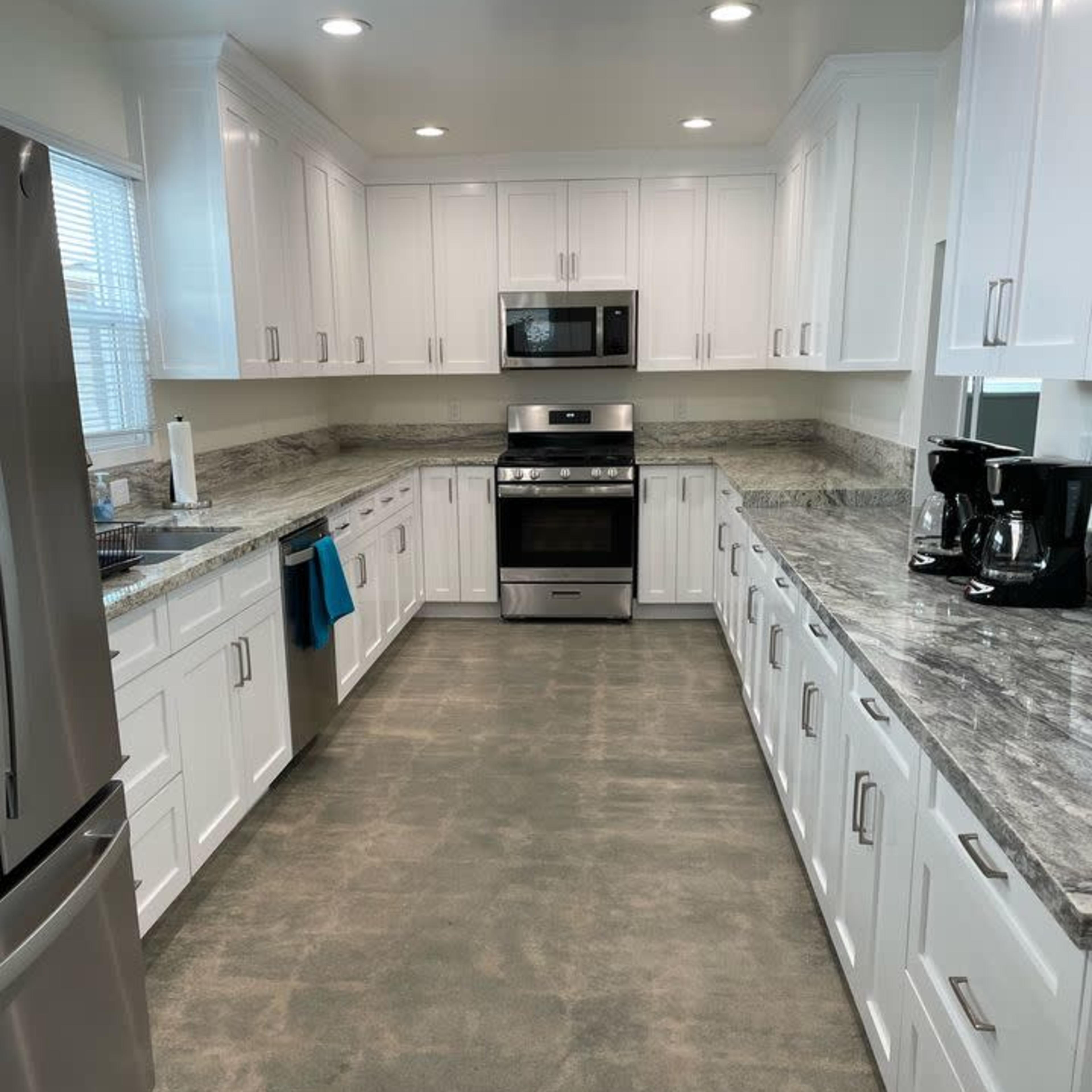 A modern kitchen with white cabinets, stainless steel appliances, and a marble countertop.
