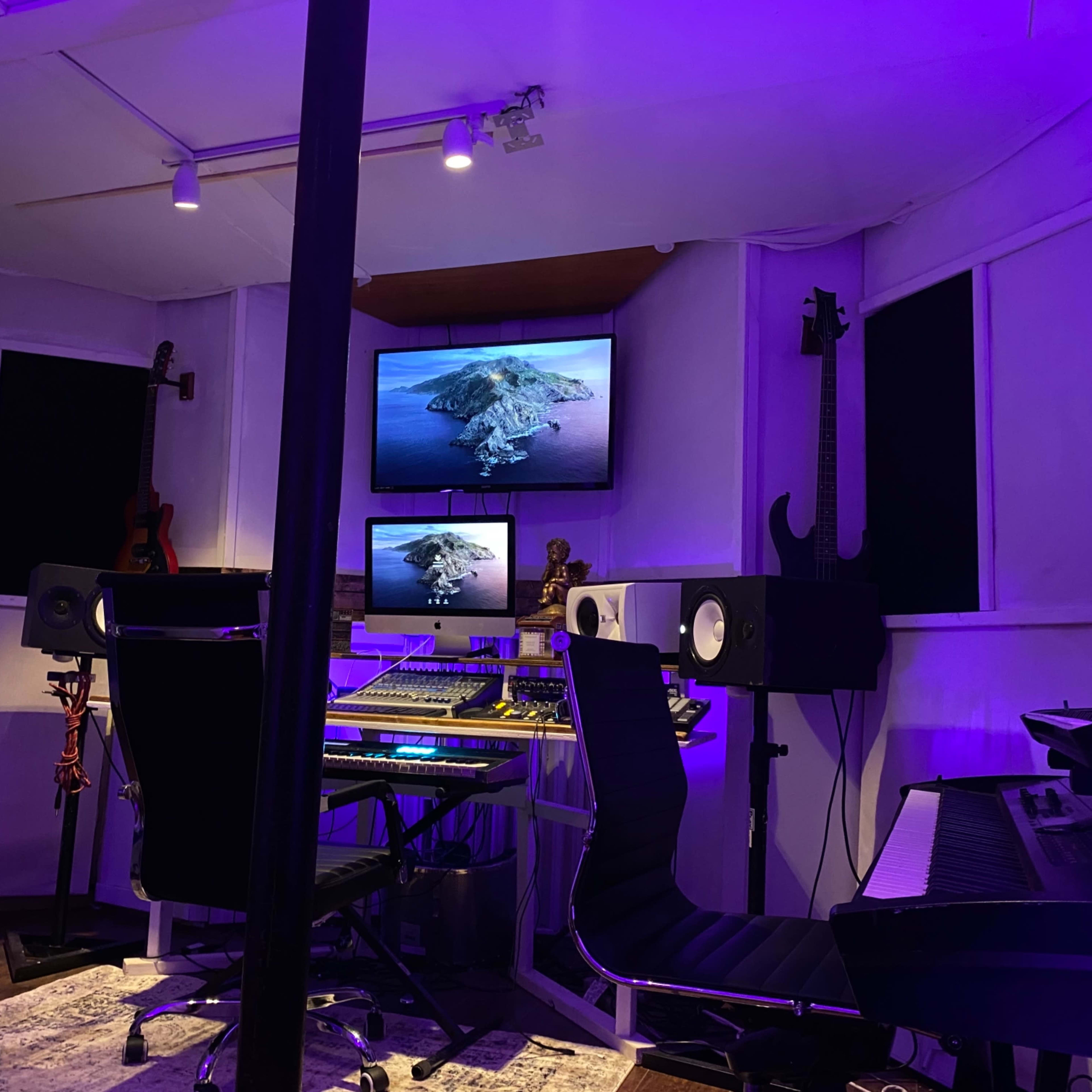 A home music studio features a digital audio workstation, monitors, and illuminated screens displaying an island view.