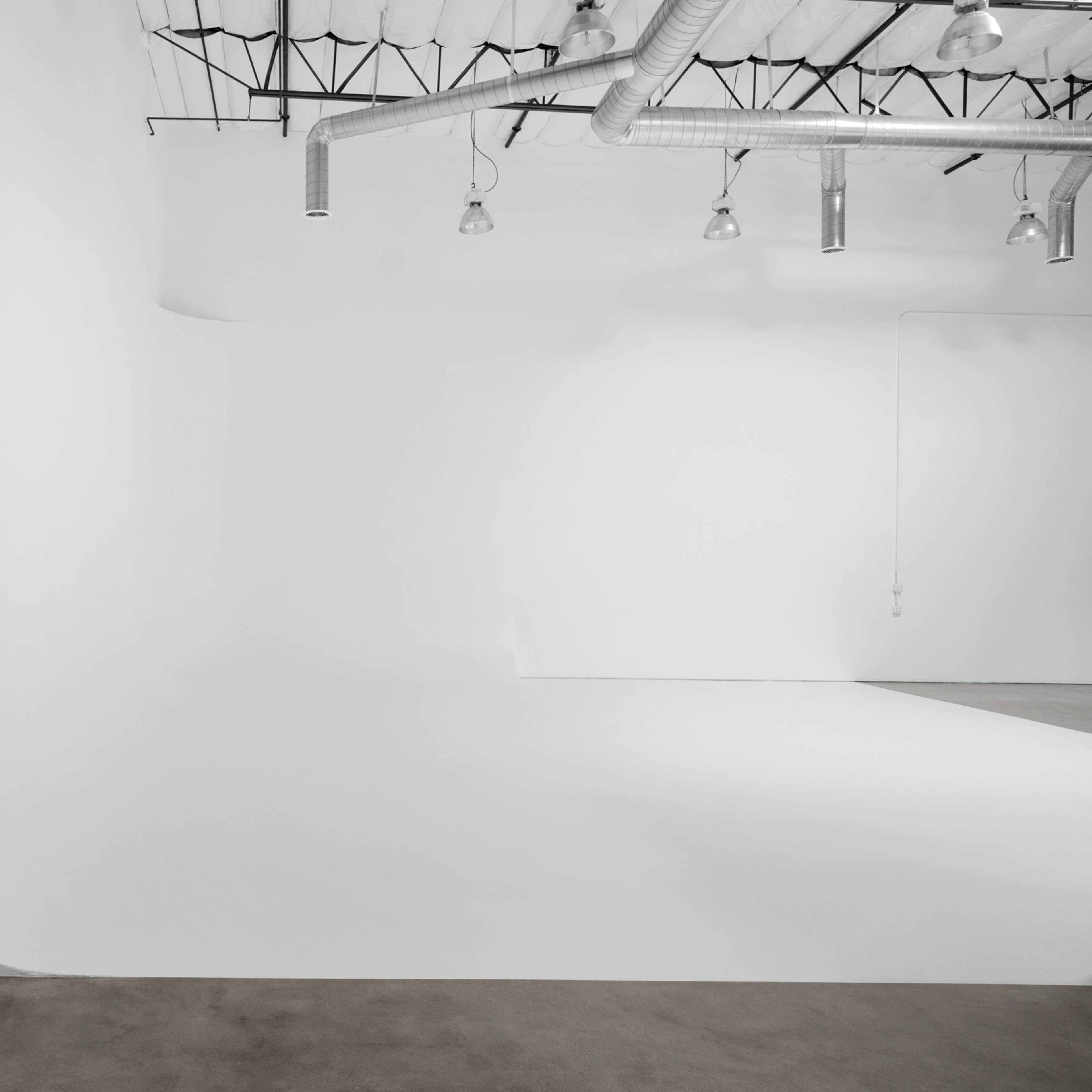 A spacious, minimalist studio with white walls, a smooth floor, and industrial lighting fixtures.