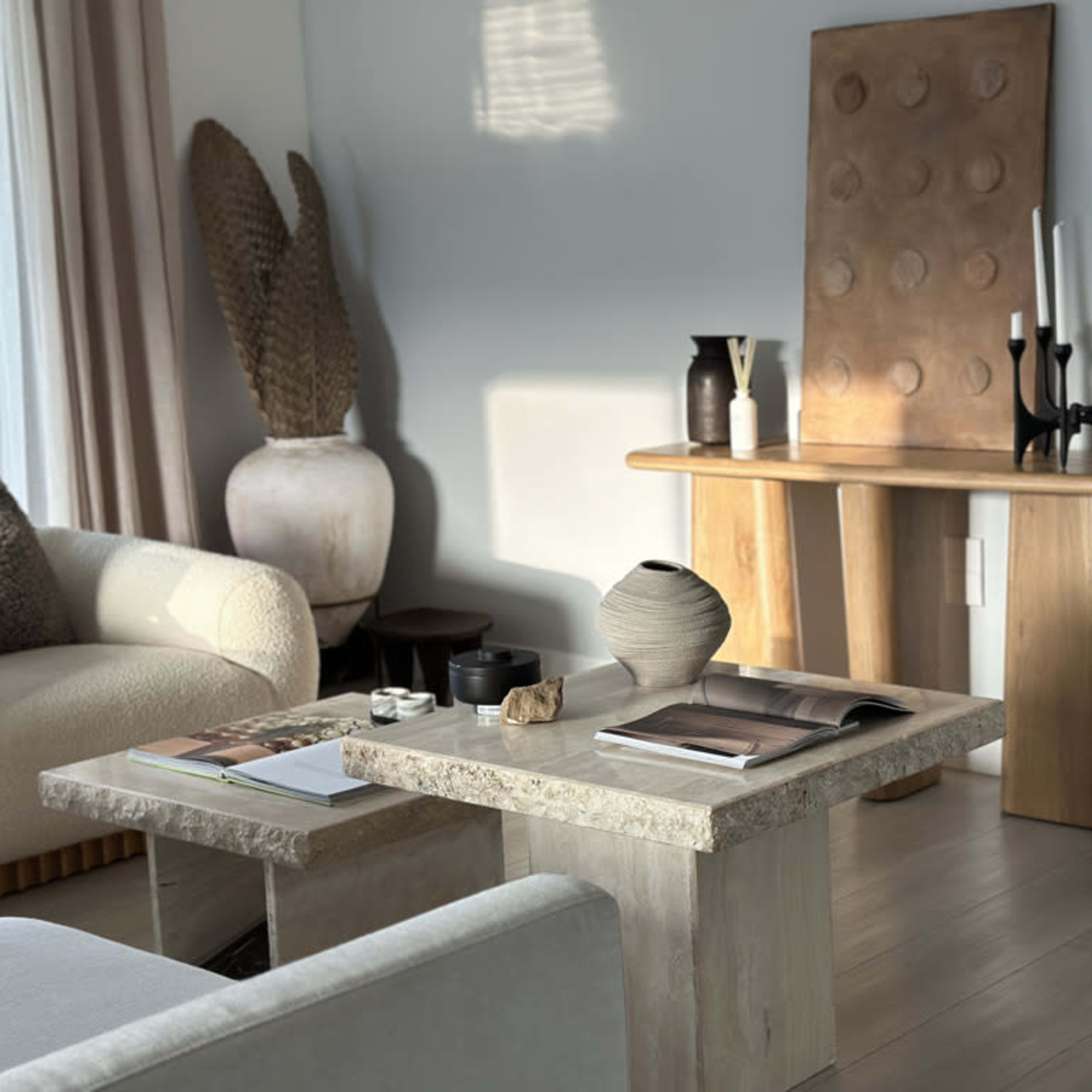 A modern living room featuring a light-colored couch, a coffee table made of stone, a wooden console table with decorative items, and a variety of vases and artwork on display.